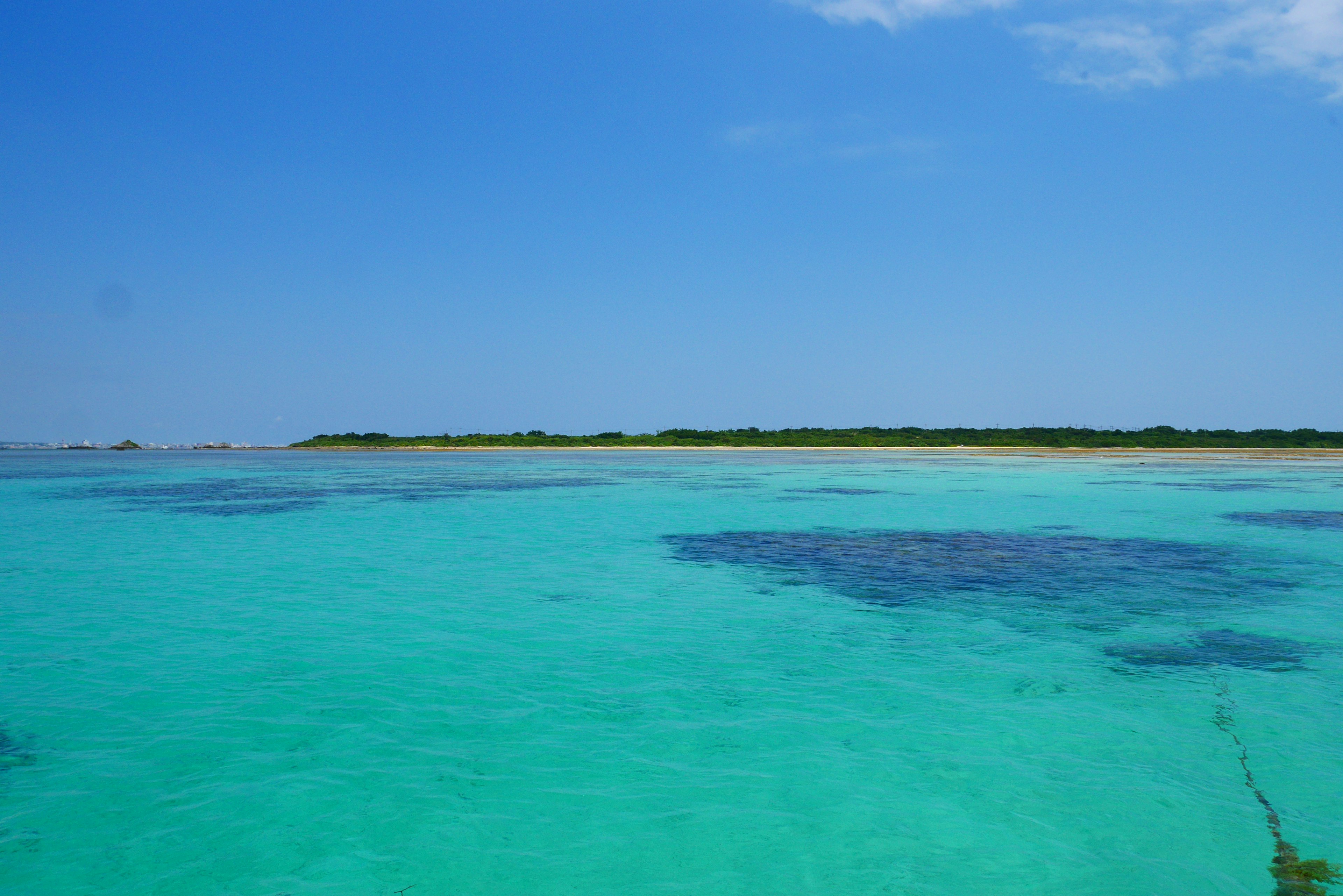 Mar turquesa vibrante bajo un cielo azul claro con islas verdes a lo lejos