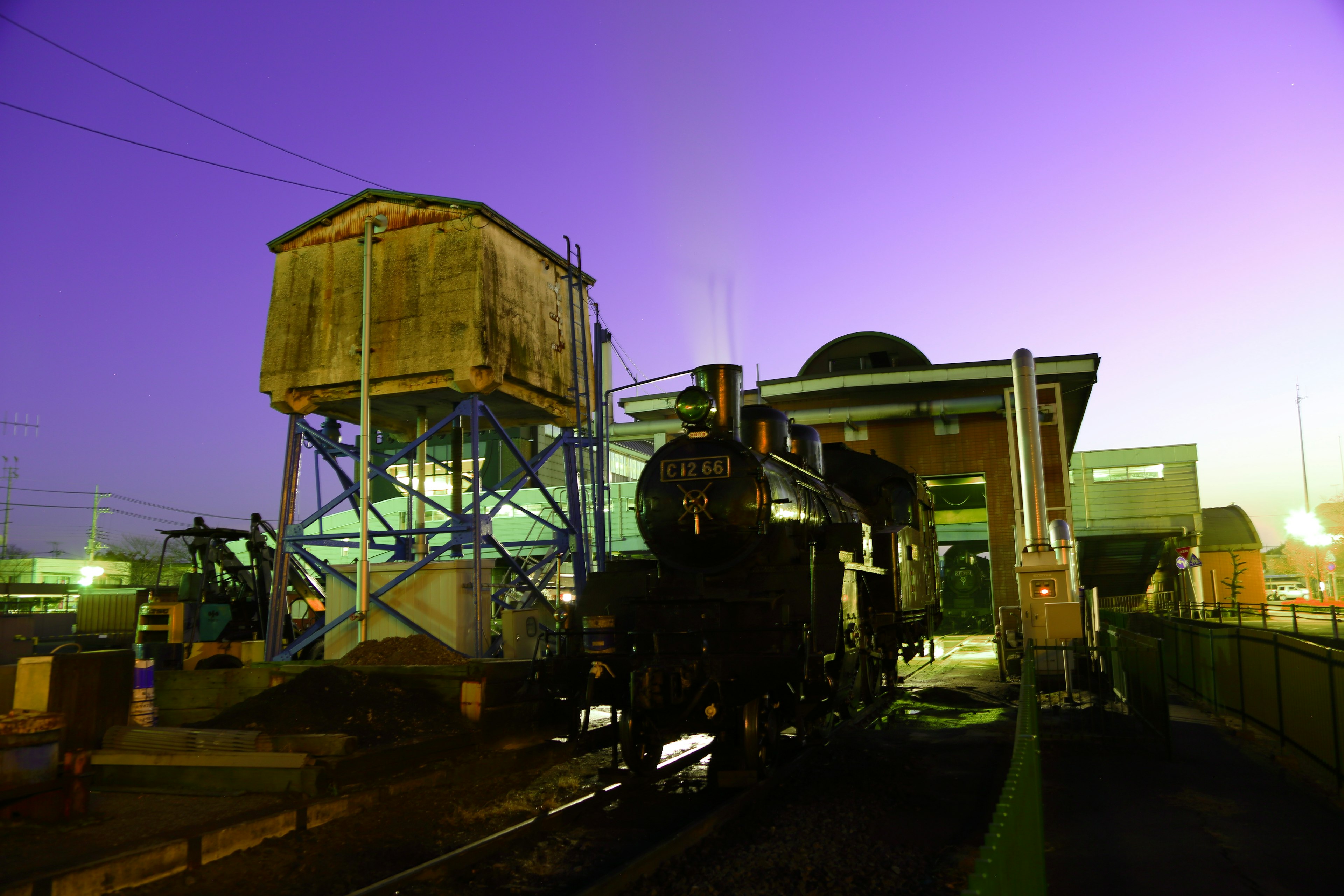 Locomotora de vapor al anochecer con edificios industriales