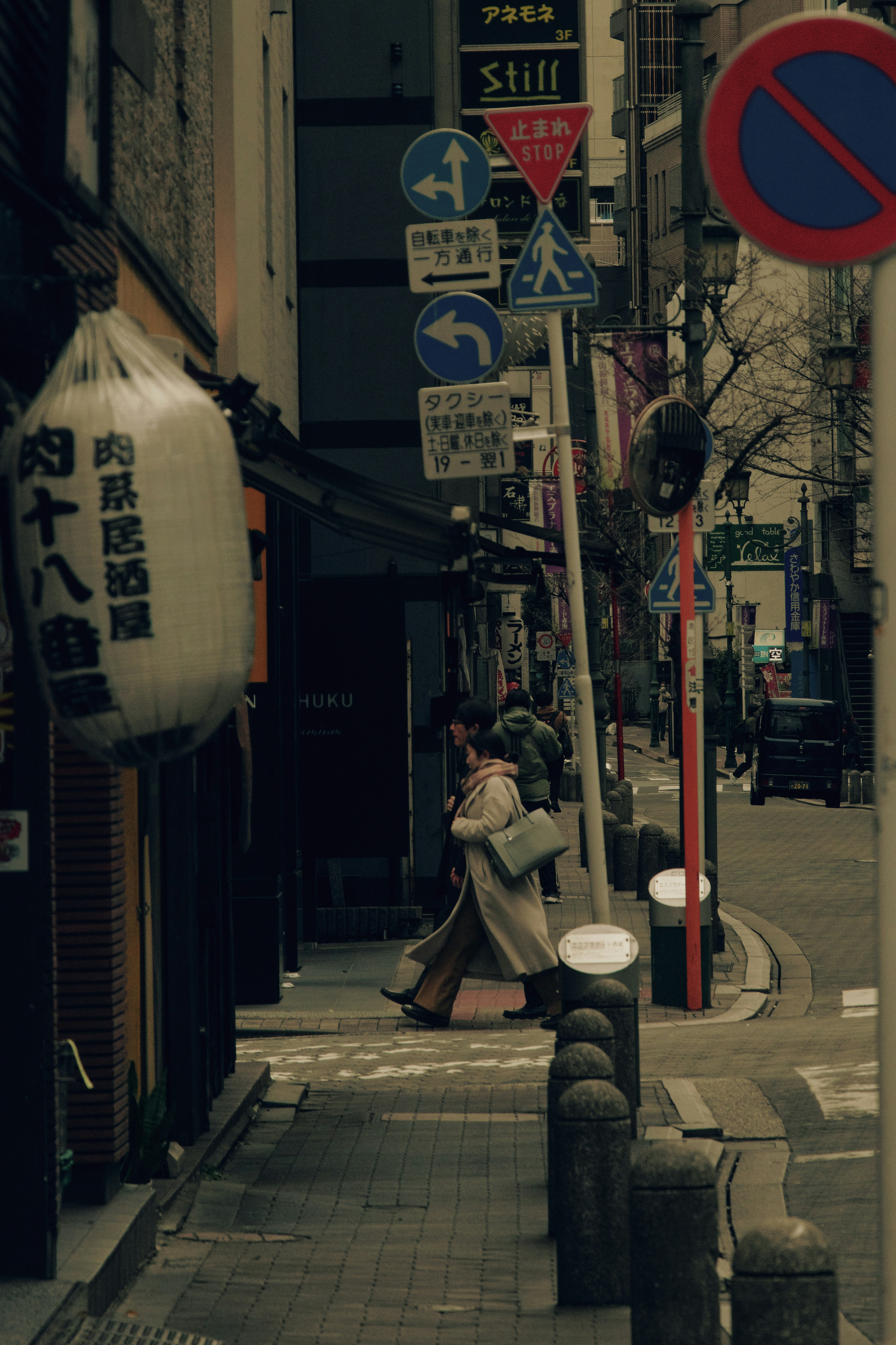 A woman walking down a narrow street with various signs