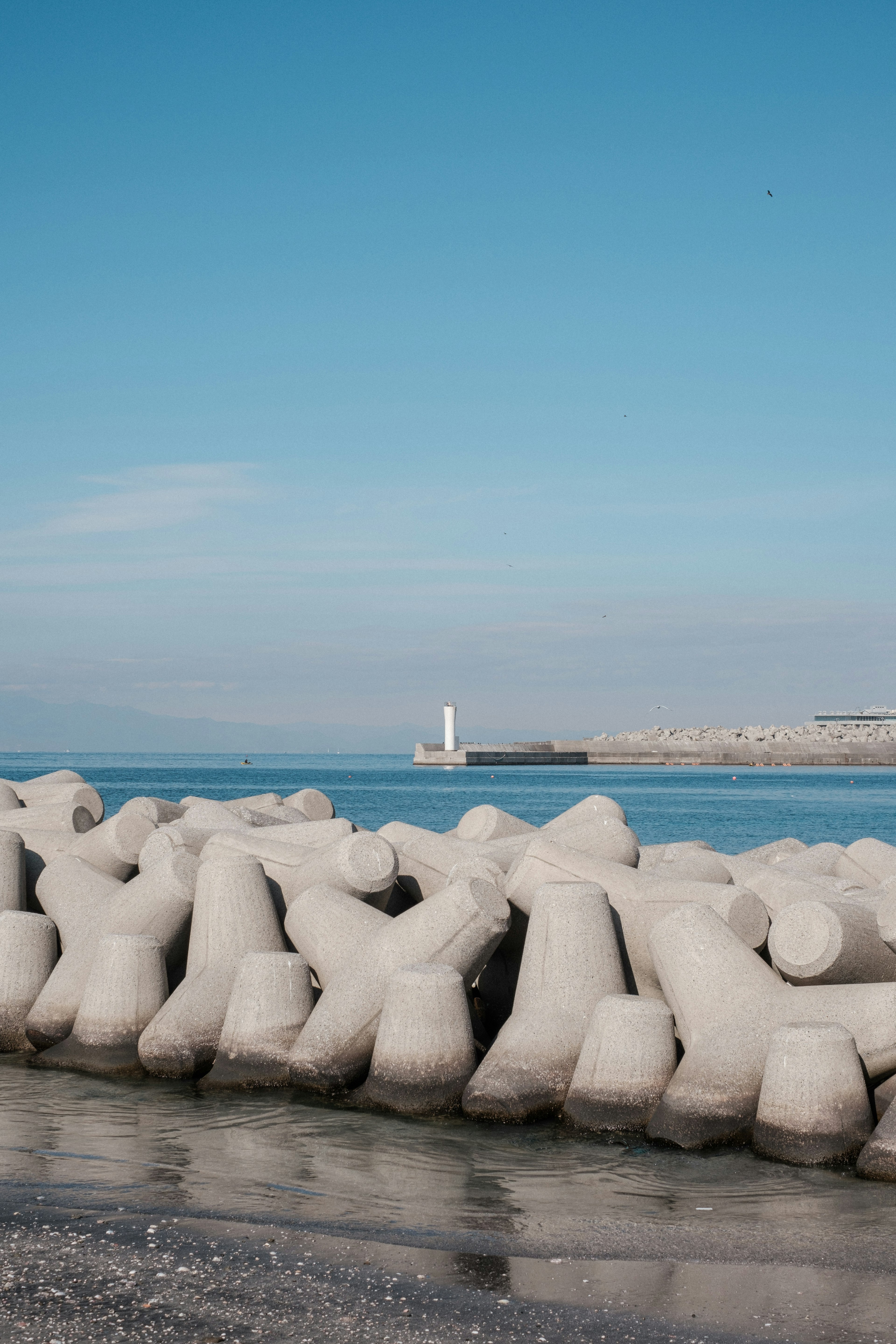 Concrete breakwater with lighthouse in the background against a blue sky