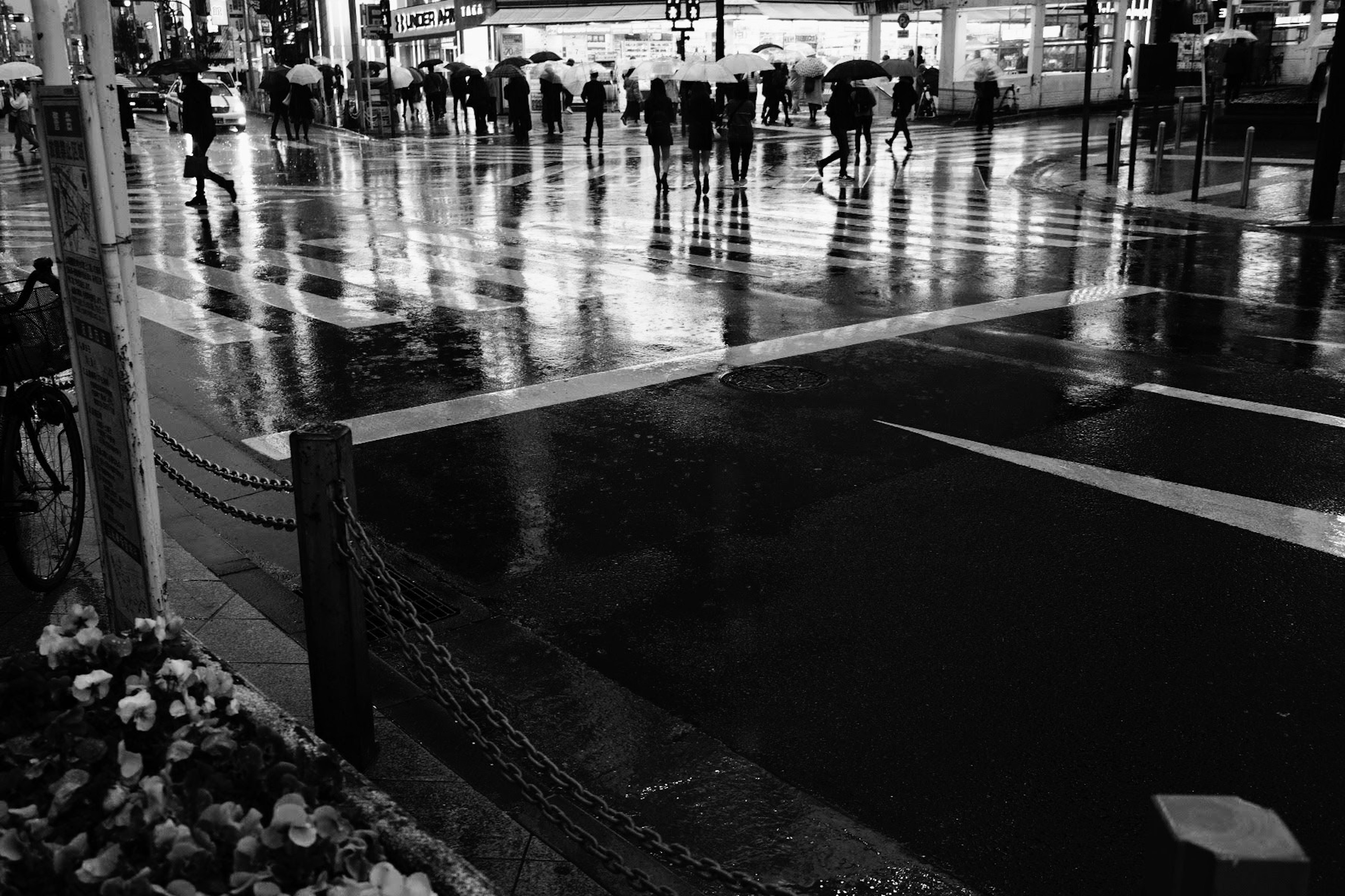 Silhouetten von Menschen an einer Straßenecke im Regen mit Reflexionen auf dem nassen Pflaster