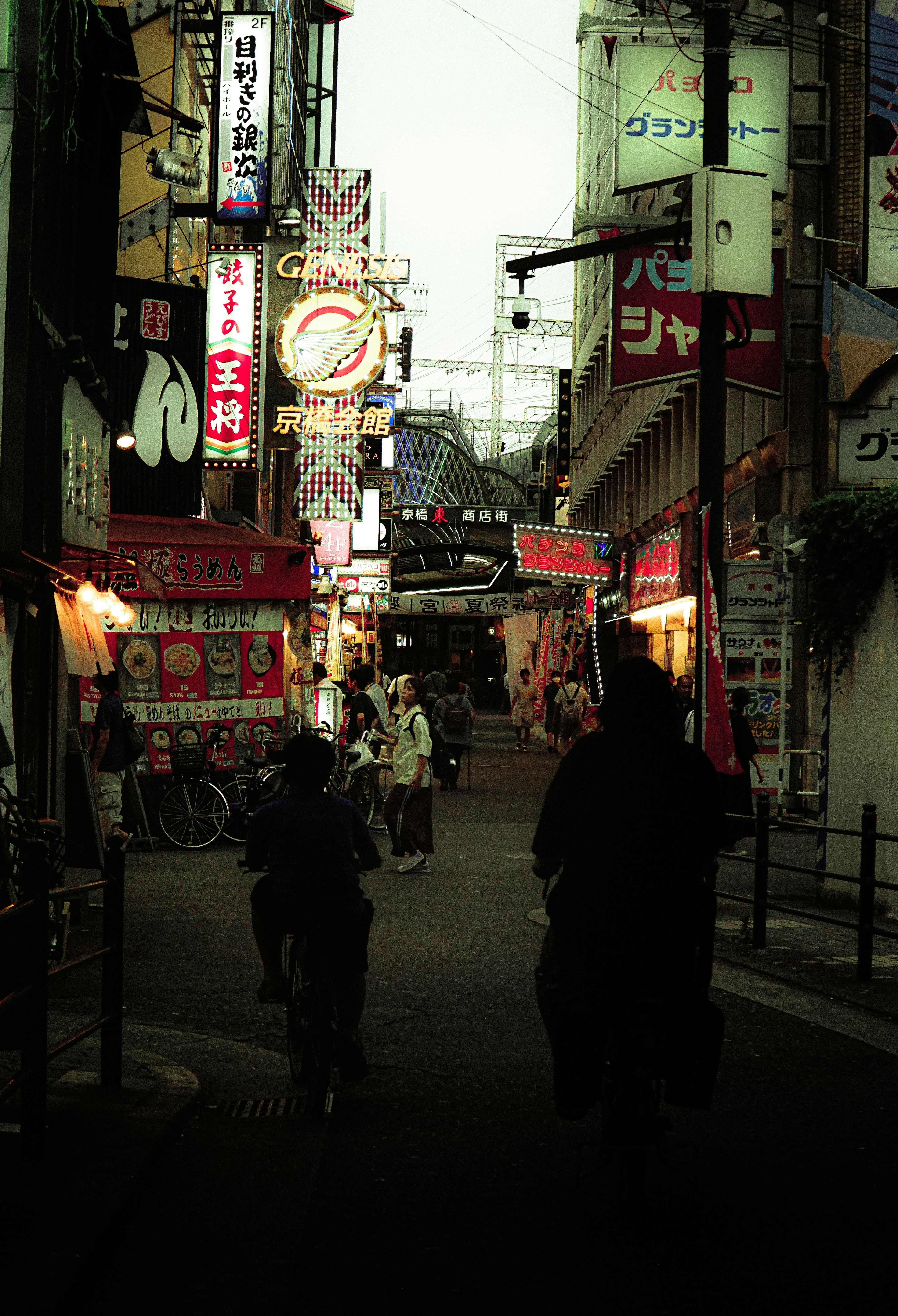 Scene of people walking in a dark alley with neon signs lining the street