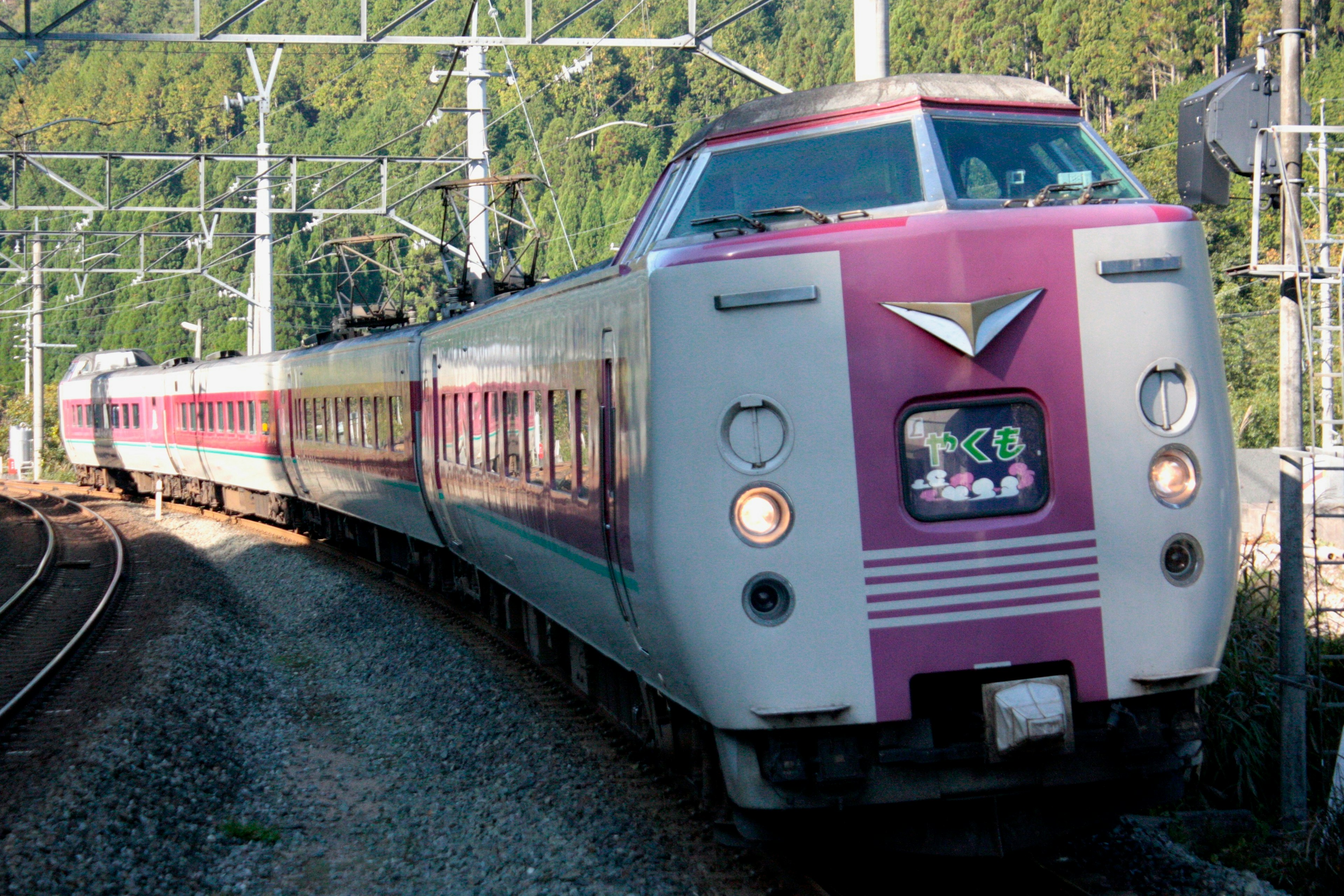 Tren expreso japonés girando en una curva con montañas verdes de fondo y vagones rosas y blancos