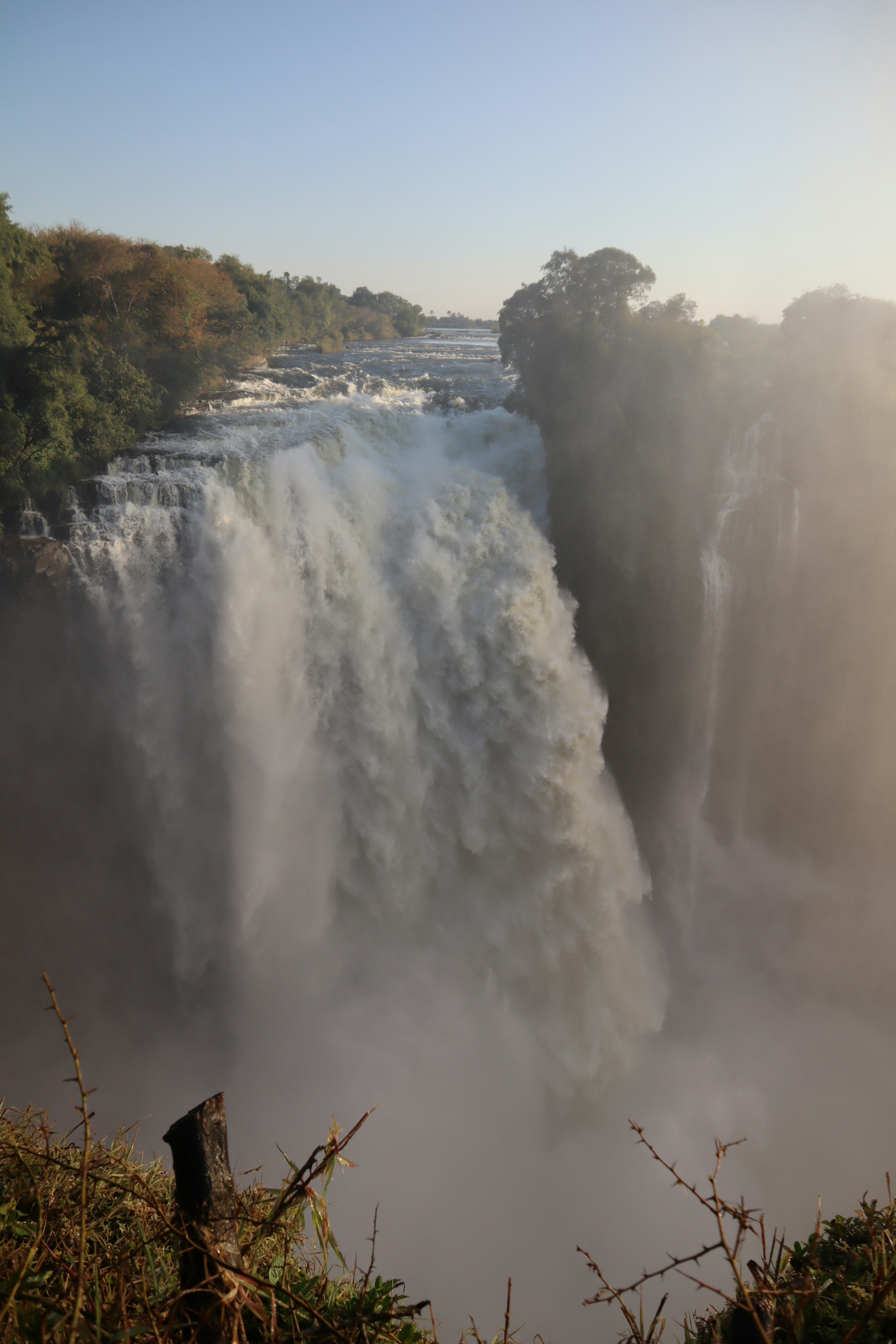 Escena de cascada majestuosa con niebla que se eleva del agua en cascada bajo un cielo azul claro