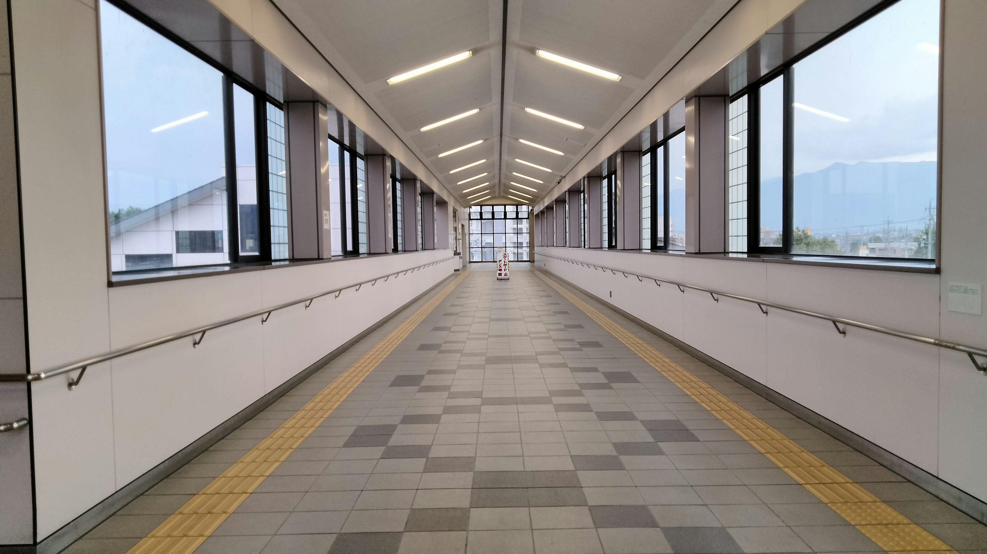 Bright corridor with large windows on both sides and tiled floor featuring yellow lines