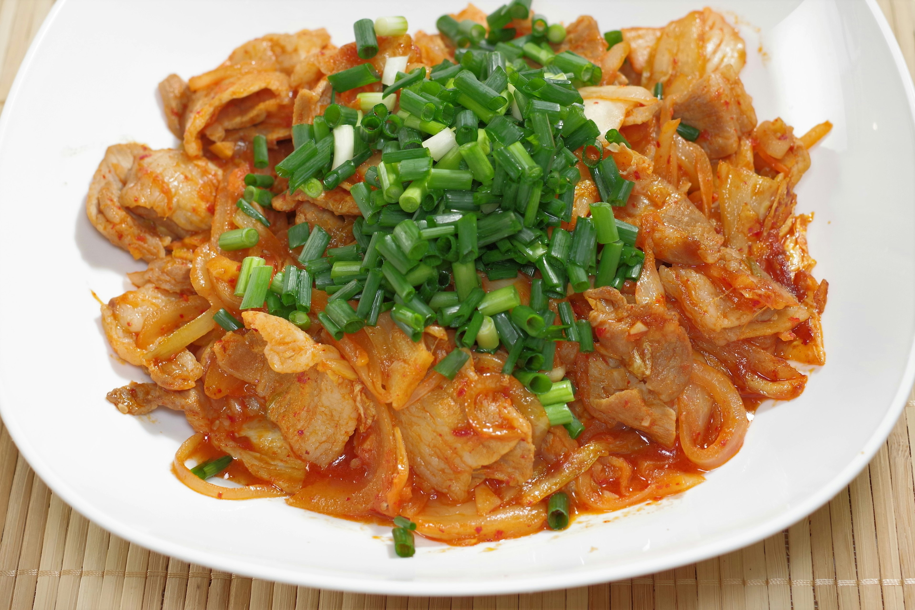 Spicy pork dish topped with green onions served on a white plate