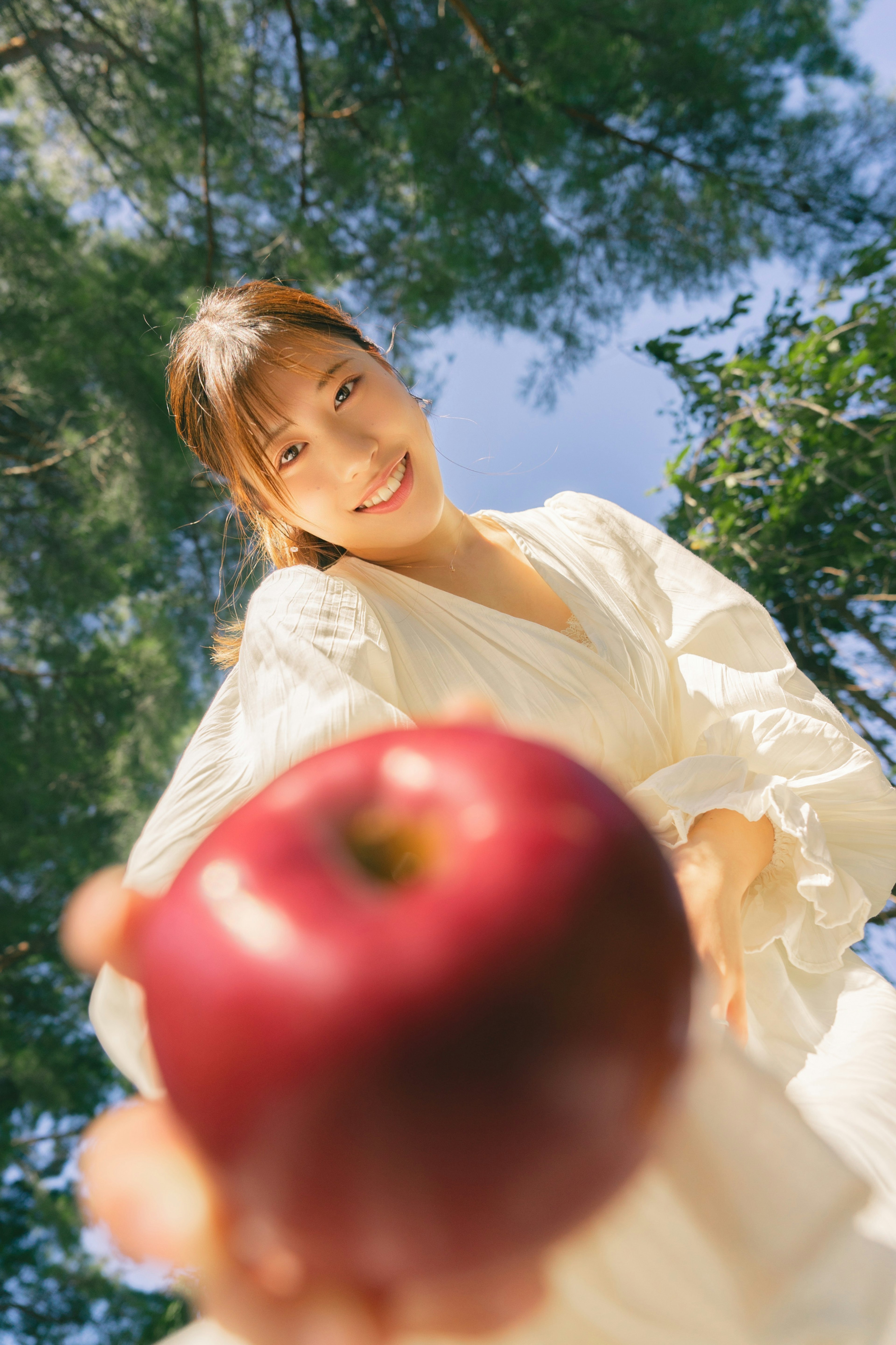 Woman in a white dress holding a red apple smiling