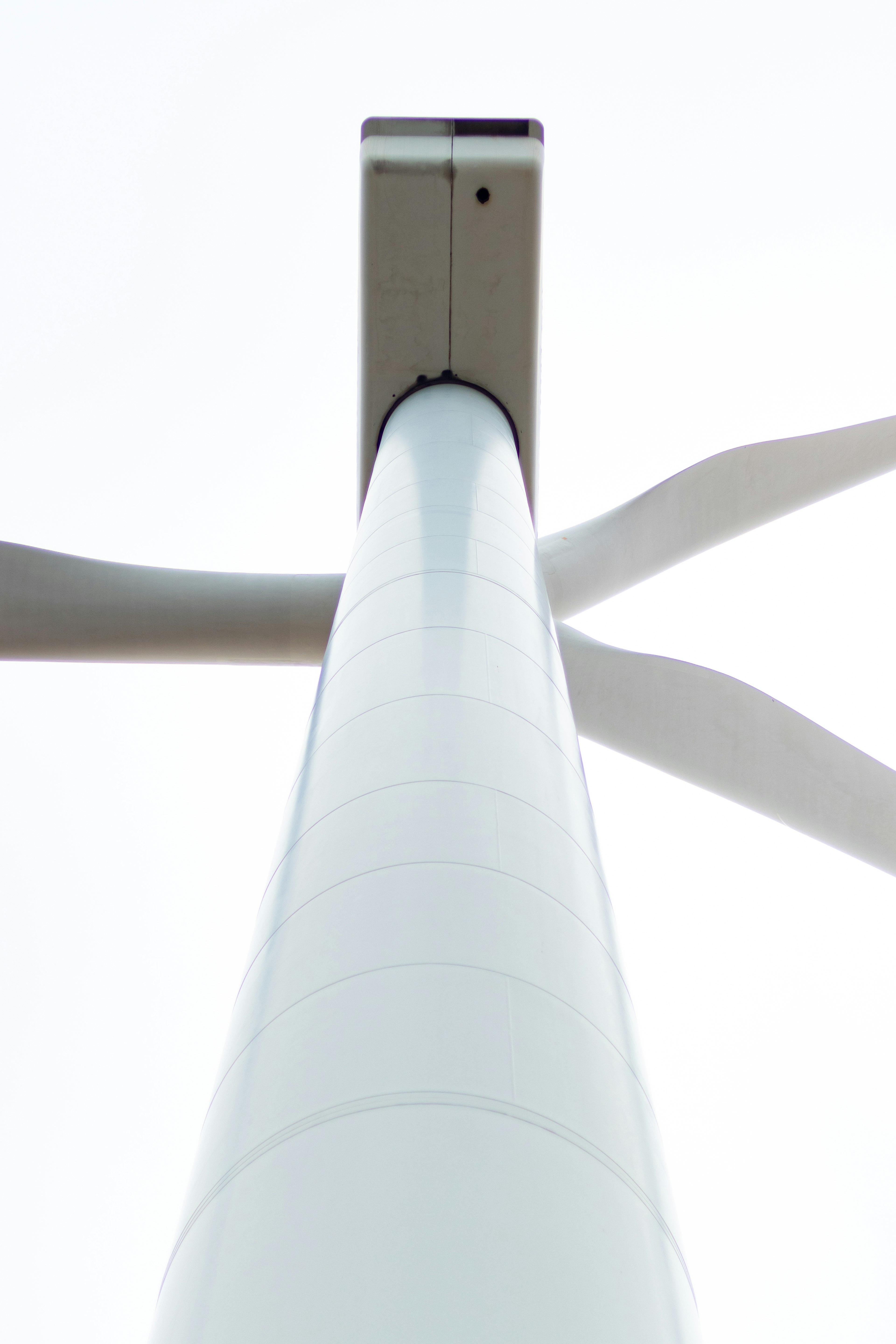 Photo looking up at a wind turbine tower White turbine blades spread out against the sky