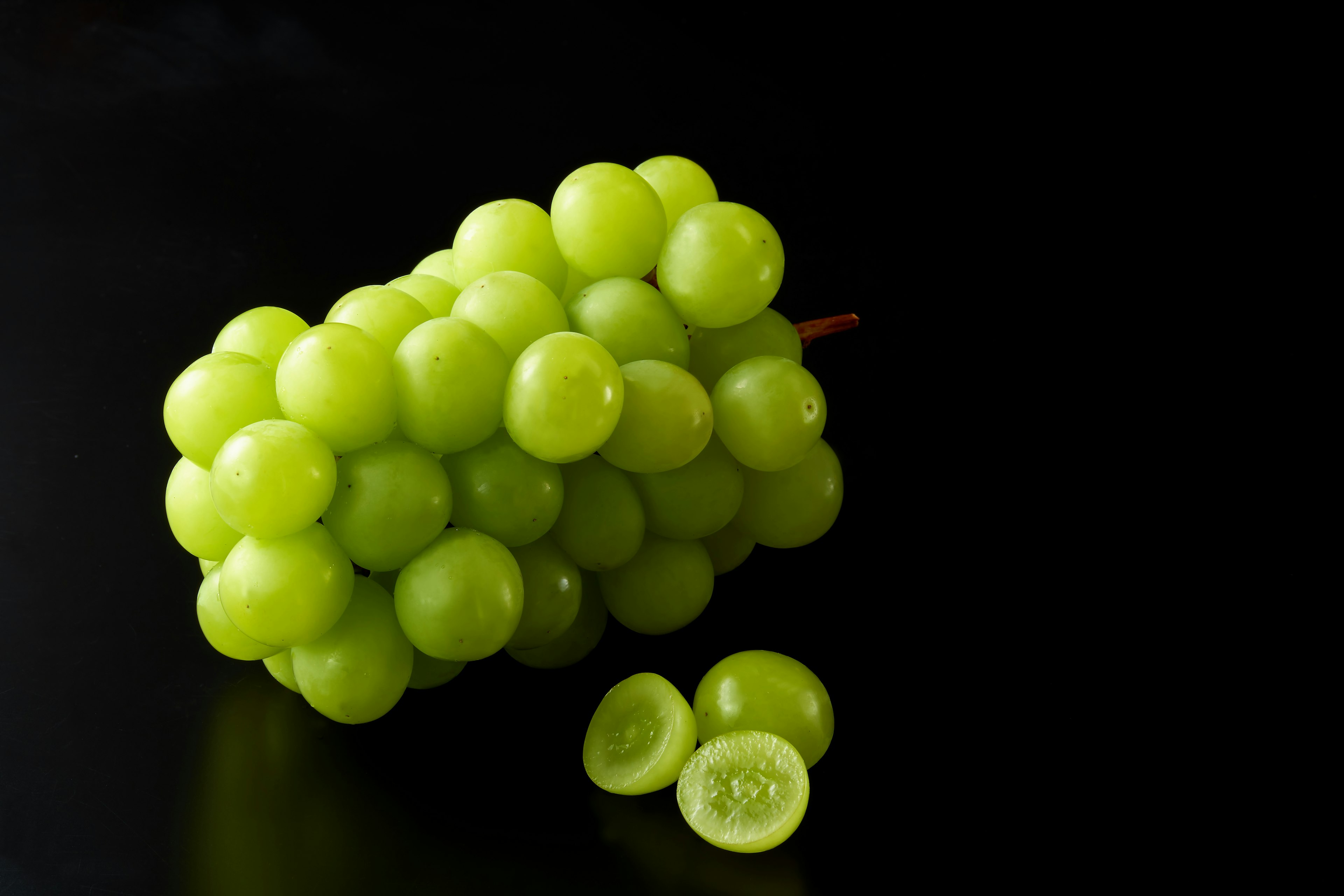 A bunch of green grapes and sliced grapes on a black background