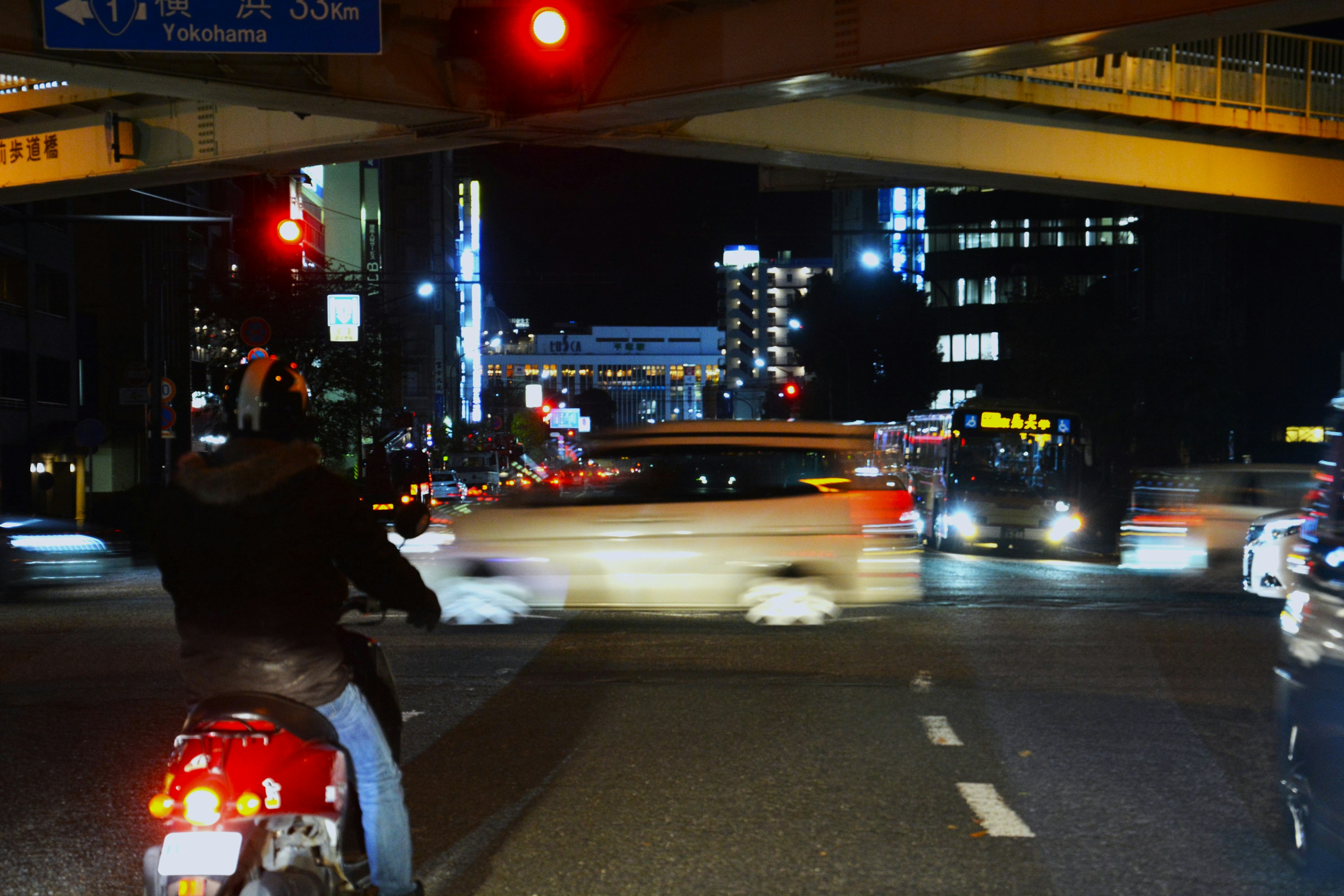 A person on a motorcycle at a city intersection with flowing car lights at night