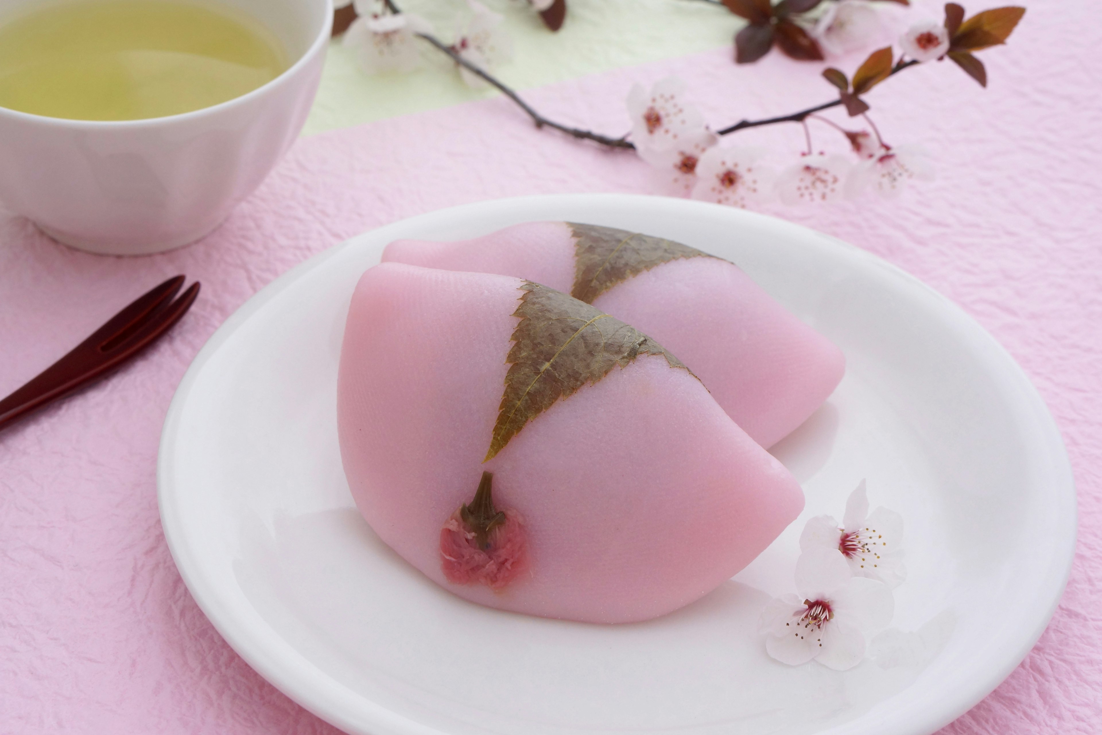 Pink Japanese dessert garnished with cherry blossoms and green tea