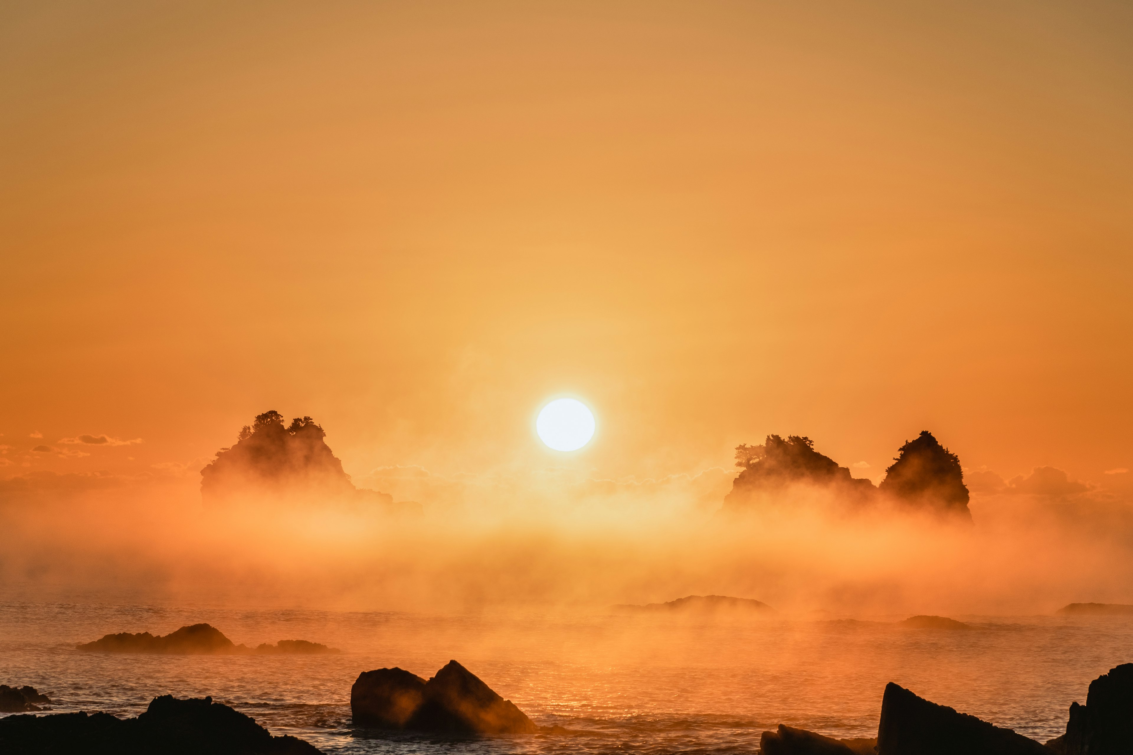 夕日の光が海と霧に反射し、岩が浮かび上がる美しい風景