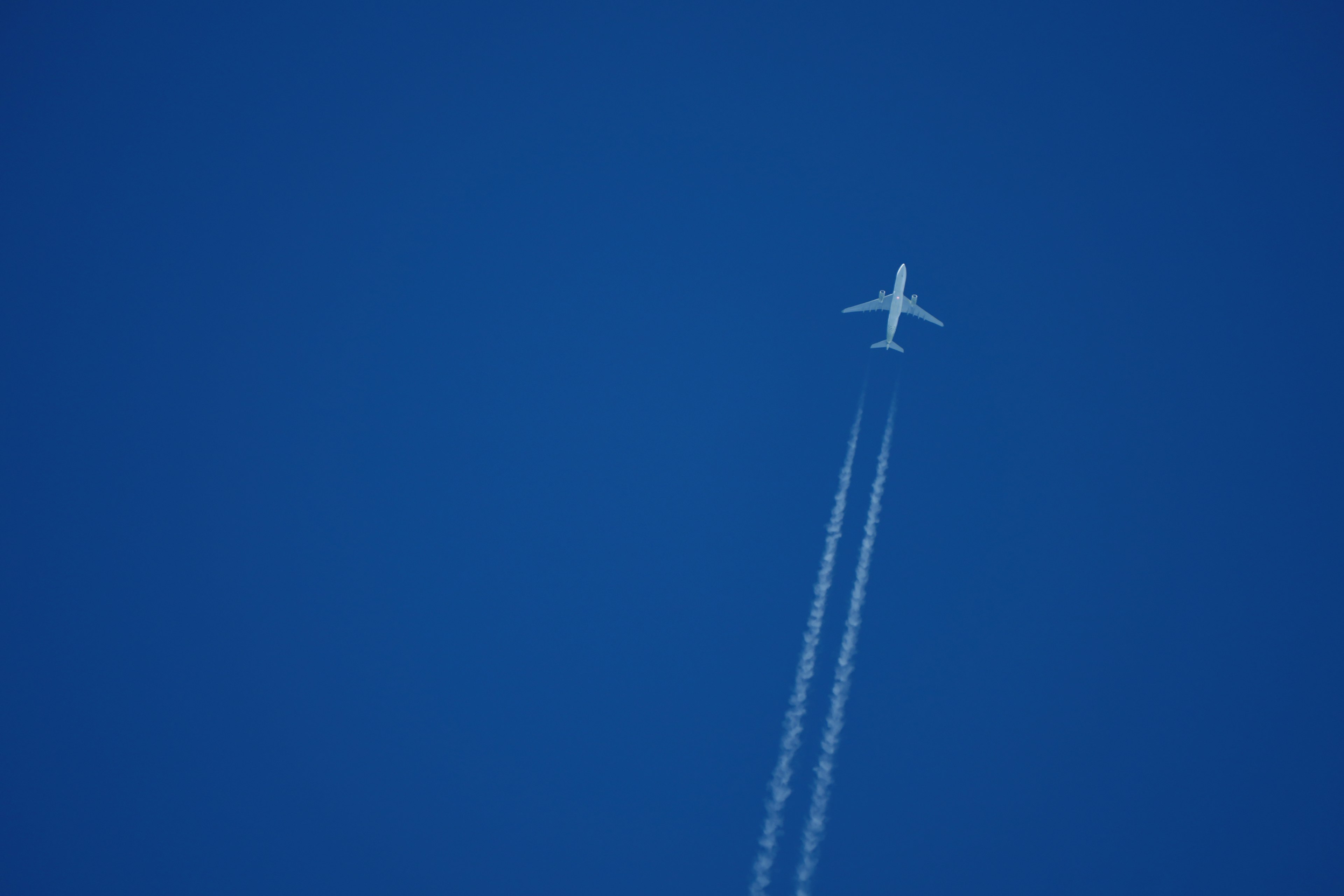 Ein Flugzeug fliegt in einem blauen Himmel mit Kondensstreifen dahinter