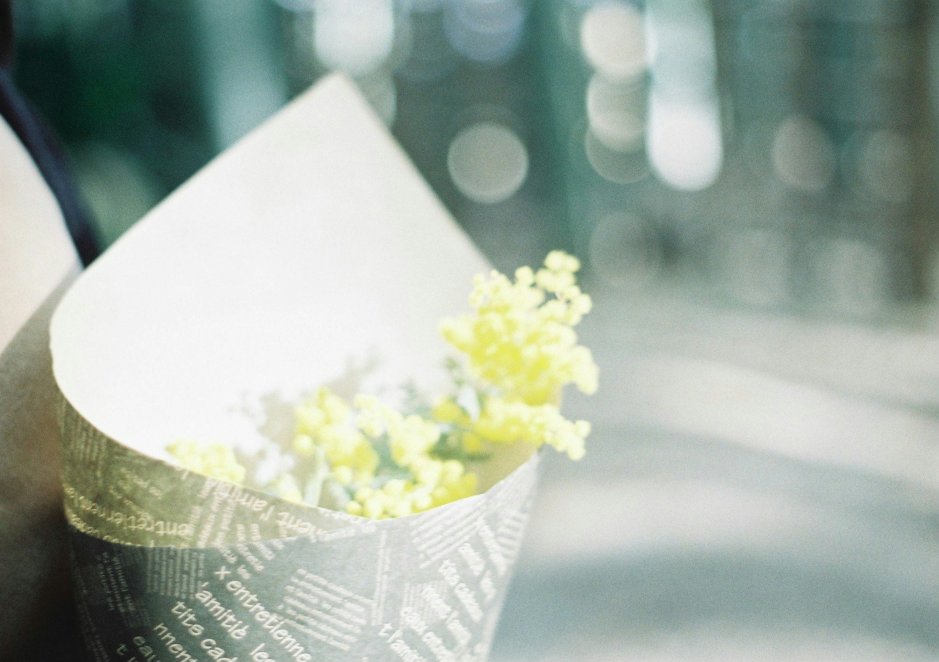 Una mano che tiene un bouquet di fiori gialli pallidi avvolto in carta decorativa