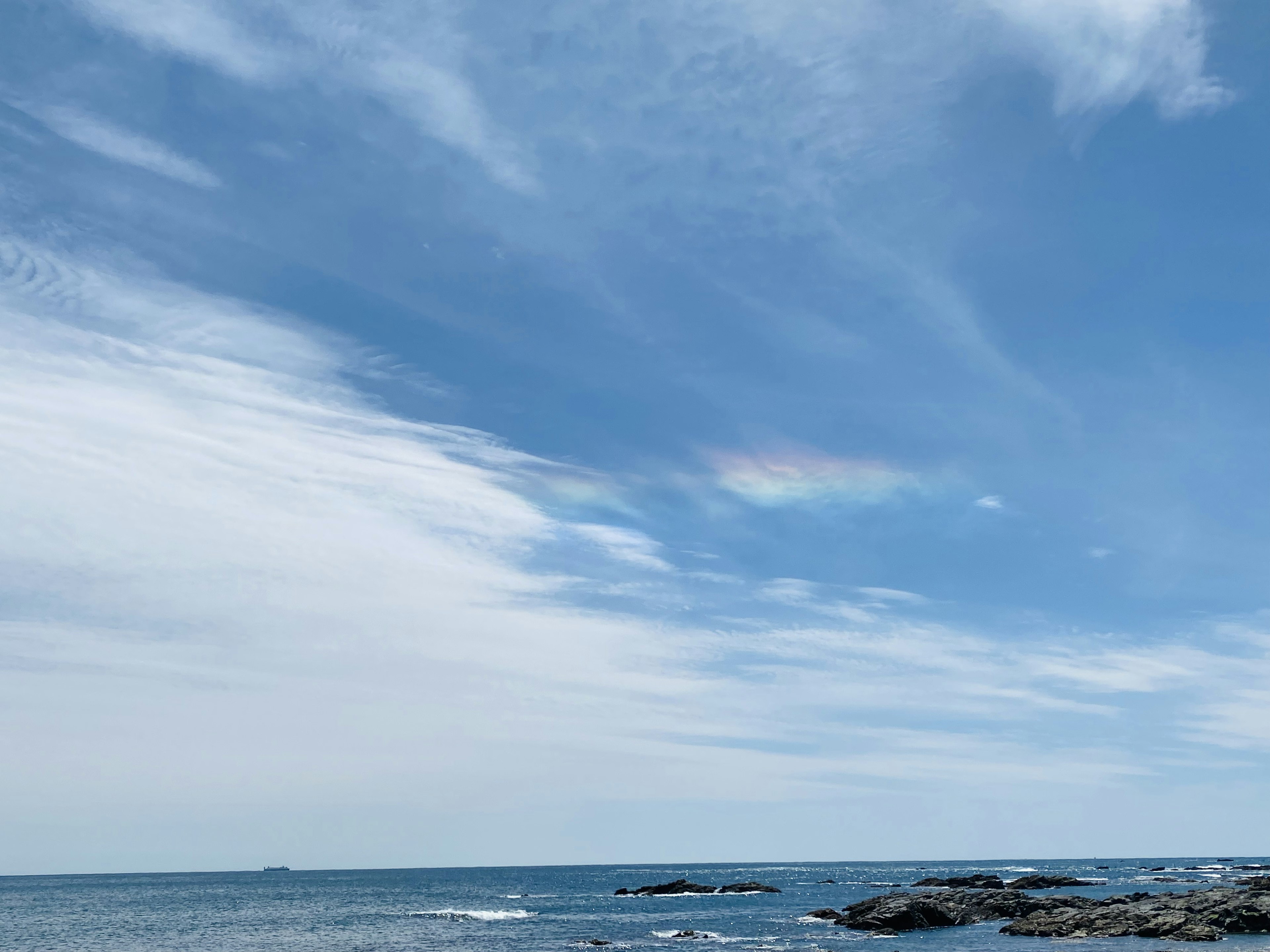 青い海と雲が広がる空に彩りを添える虹