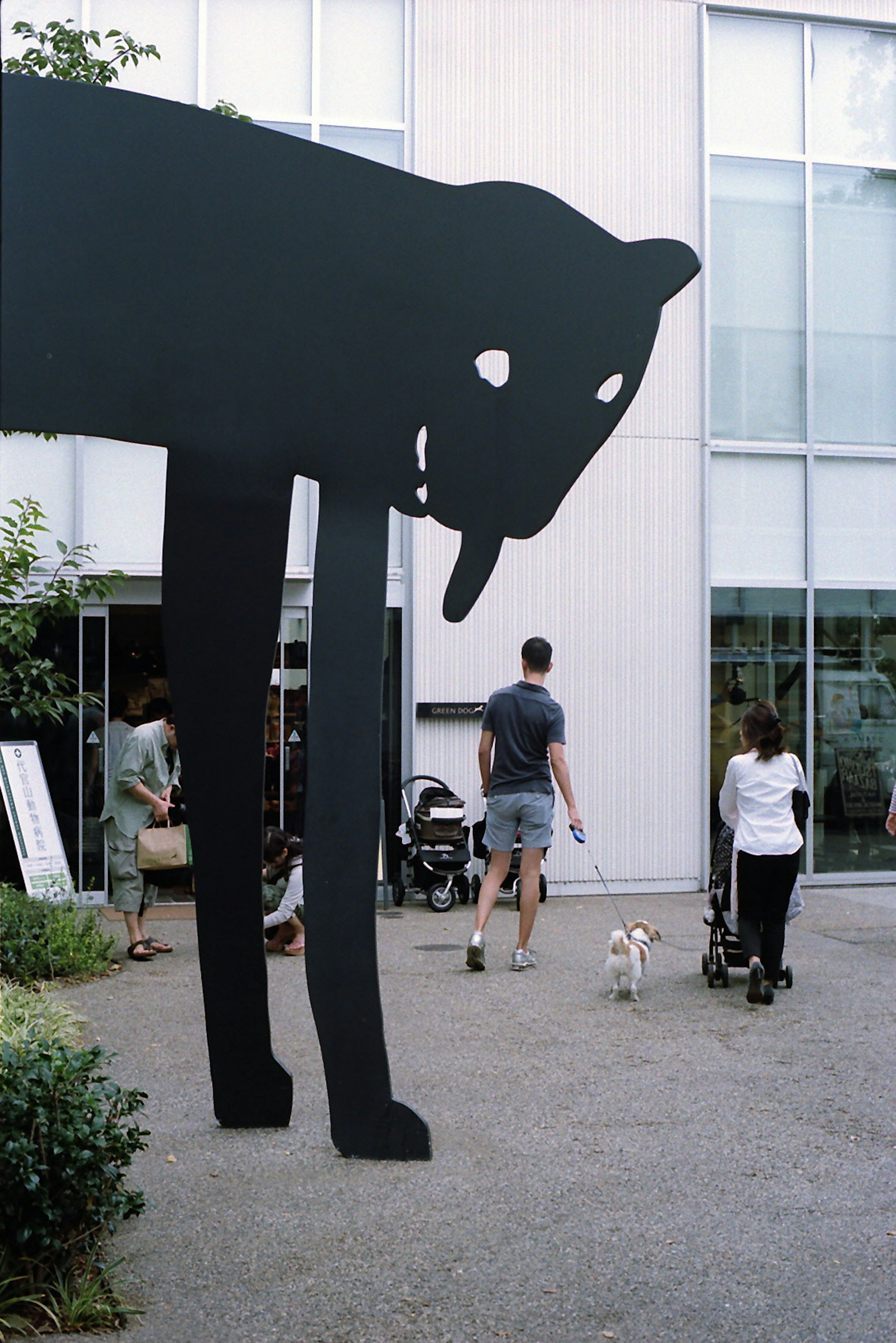 A large black dog sculpture stands while people walk by