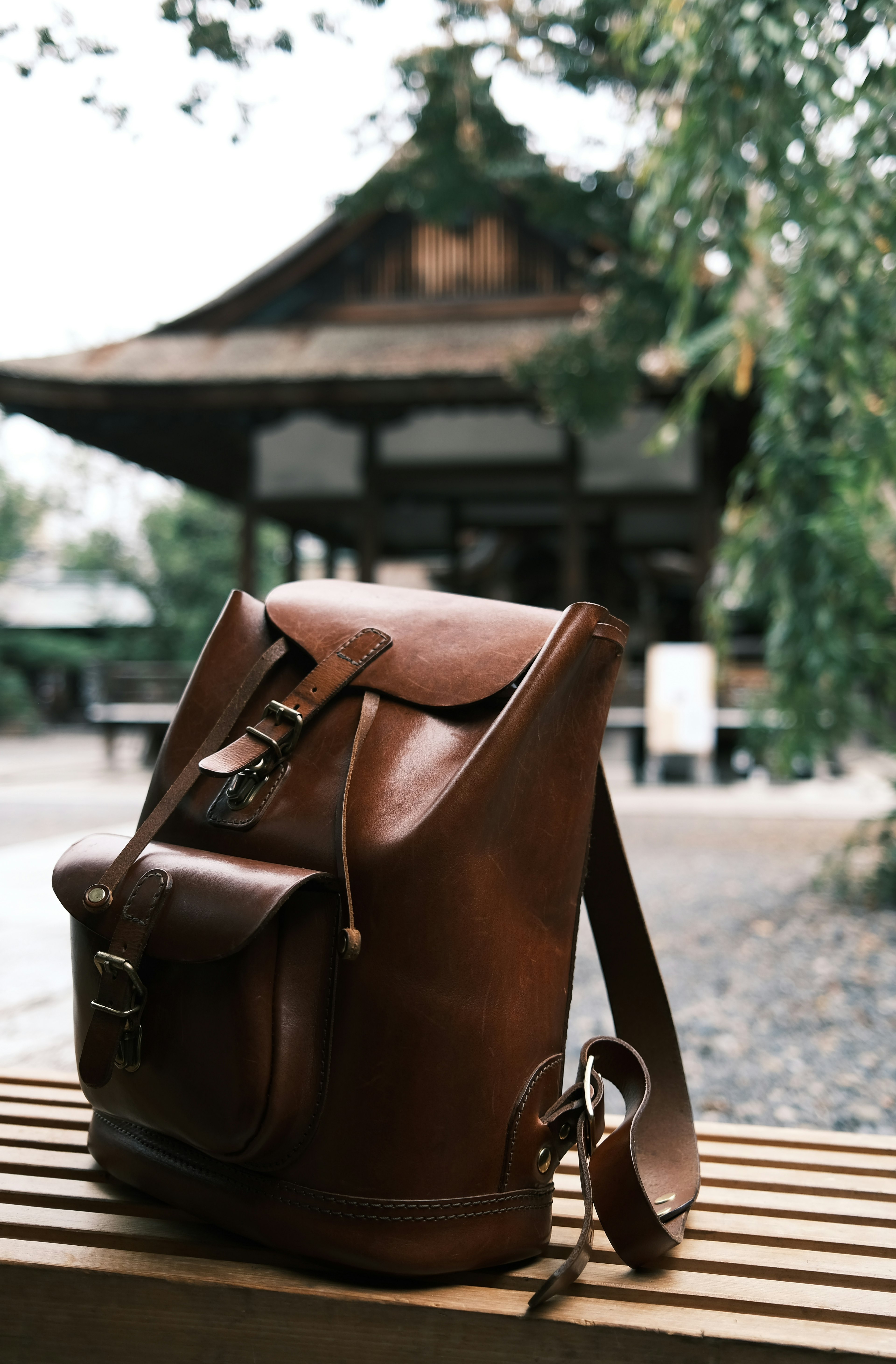 Mochila de cuero marrón colocada sobre un banco de madera con un edificio tradicional al fondo