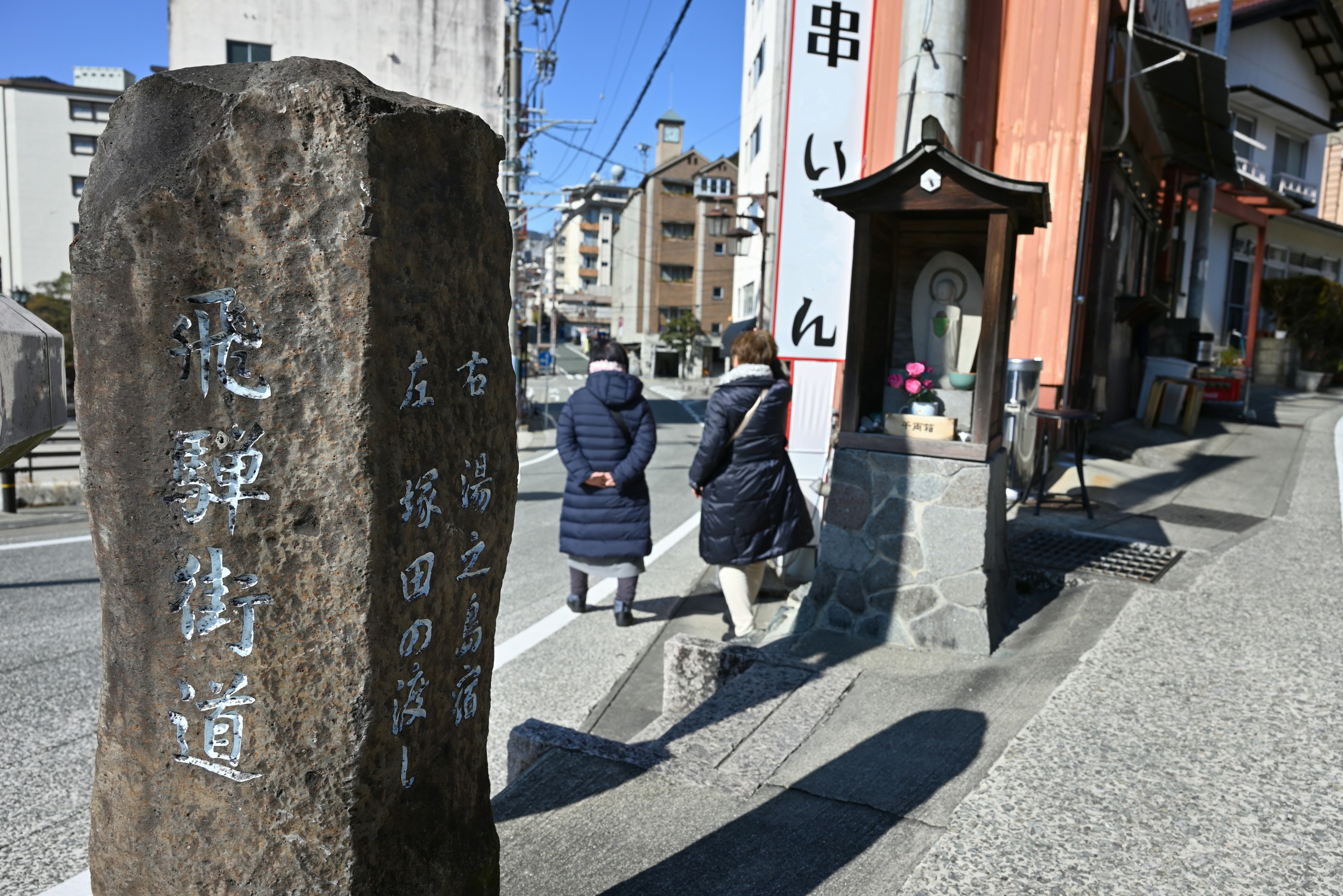 古い石の標識と通行人の姿が見える街道の風景