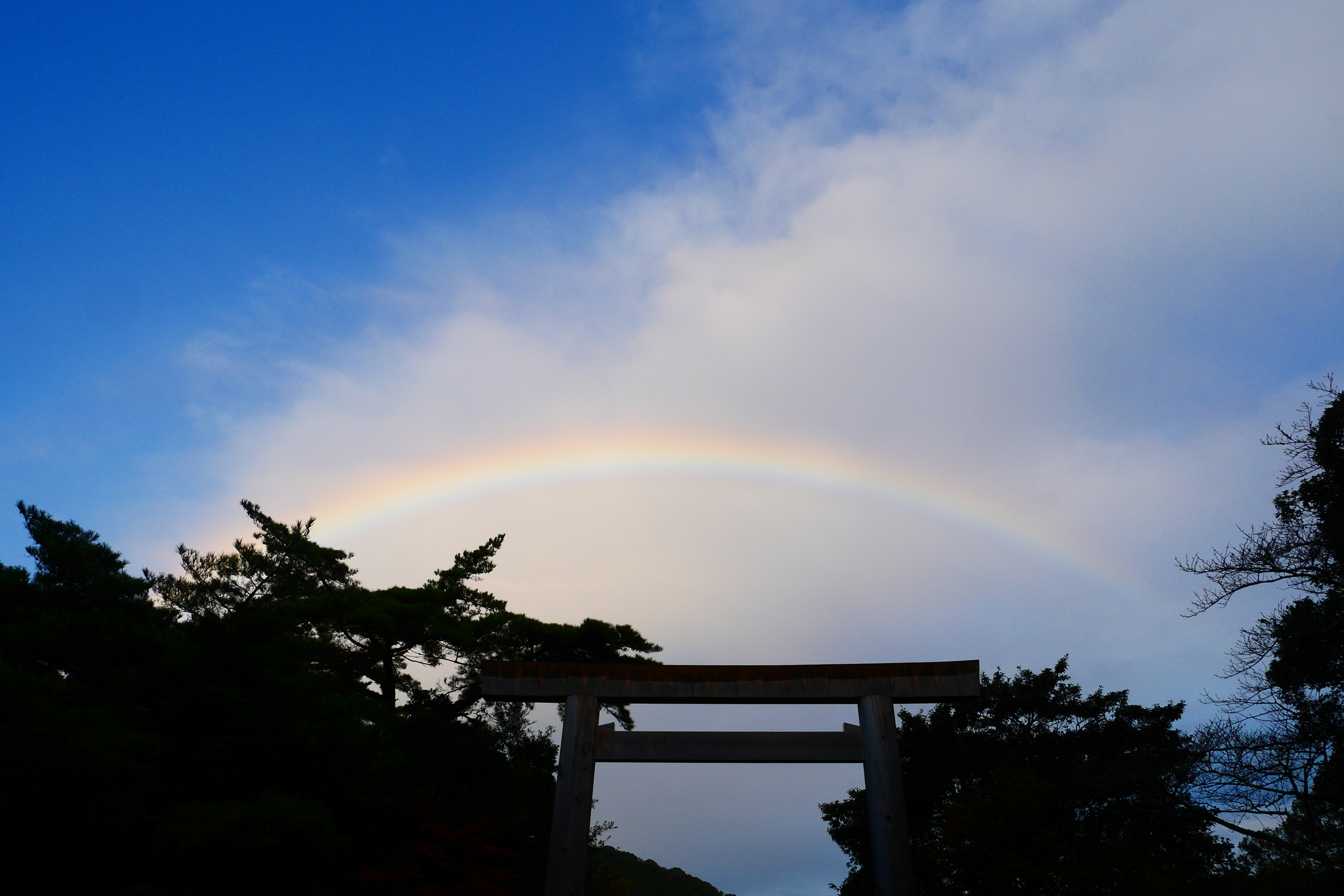 Silhouette di un torii con un arcobaleno nel cielo blu