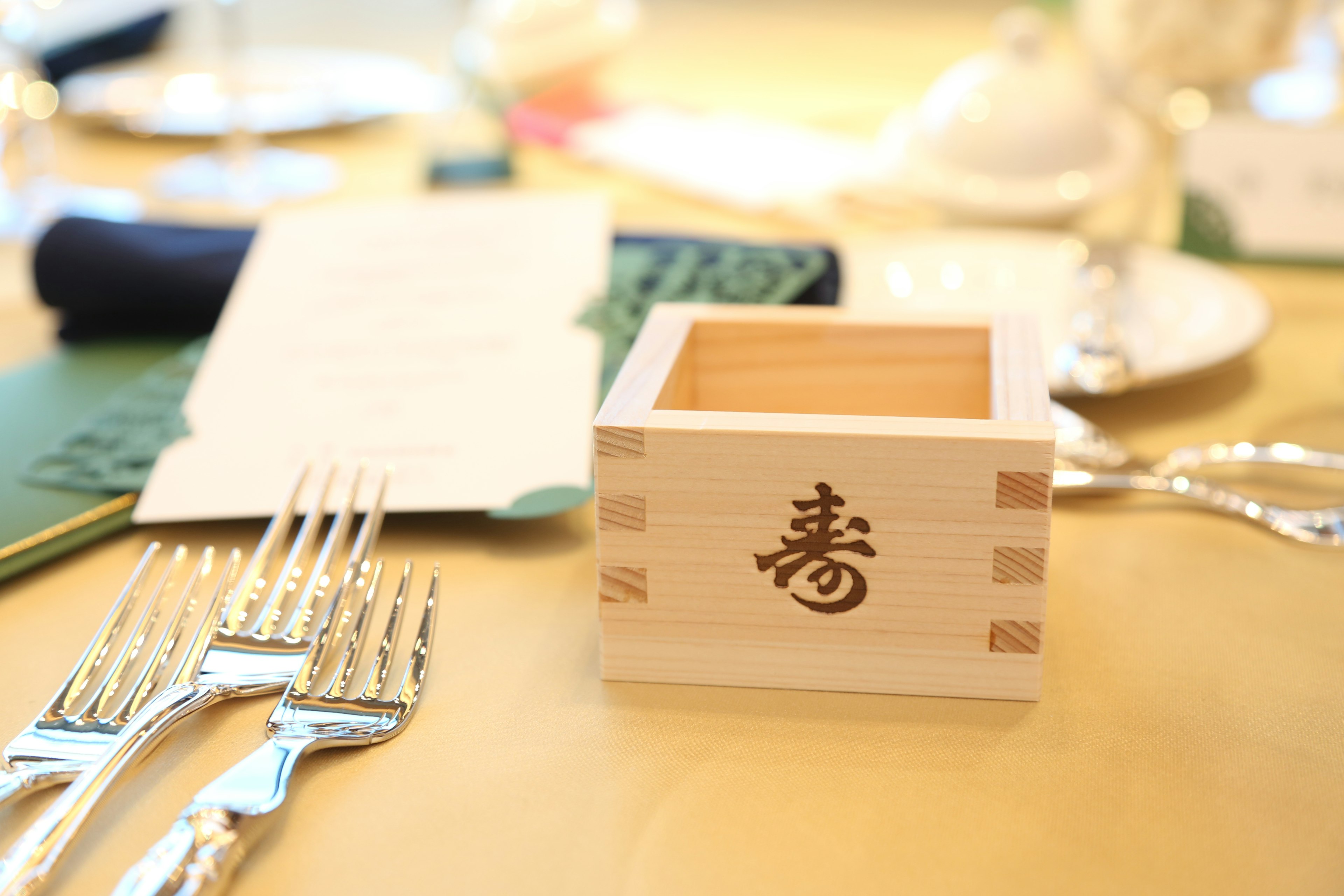 A wooden box with the kanji character for longevity on a dining table setting