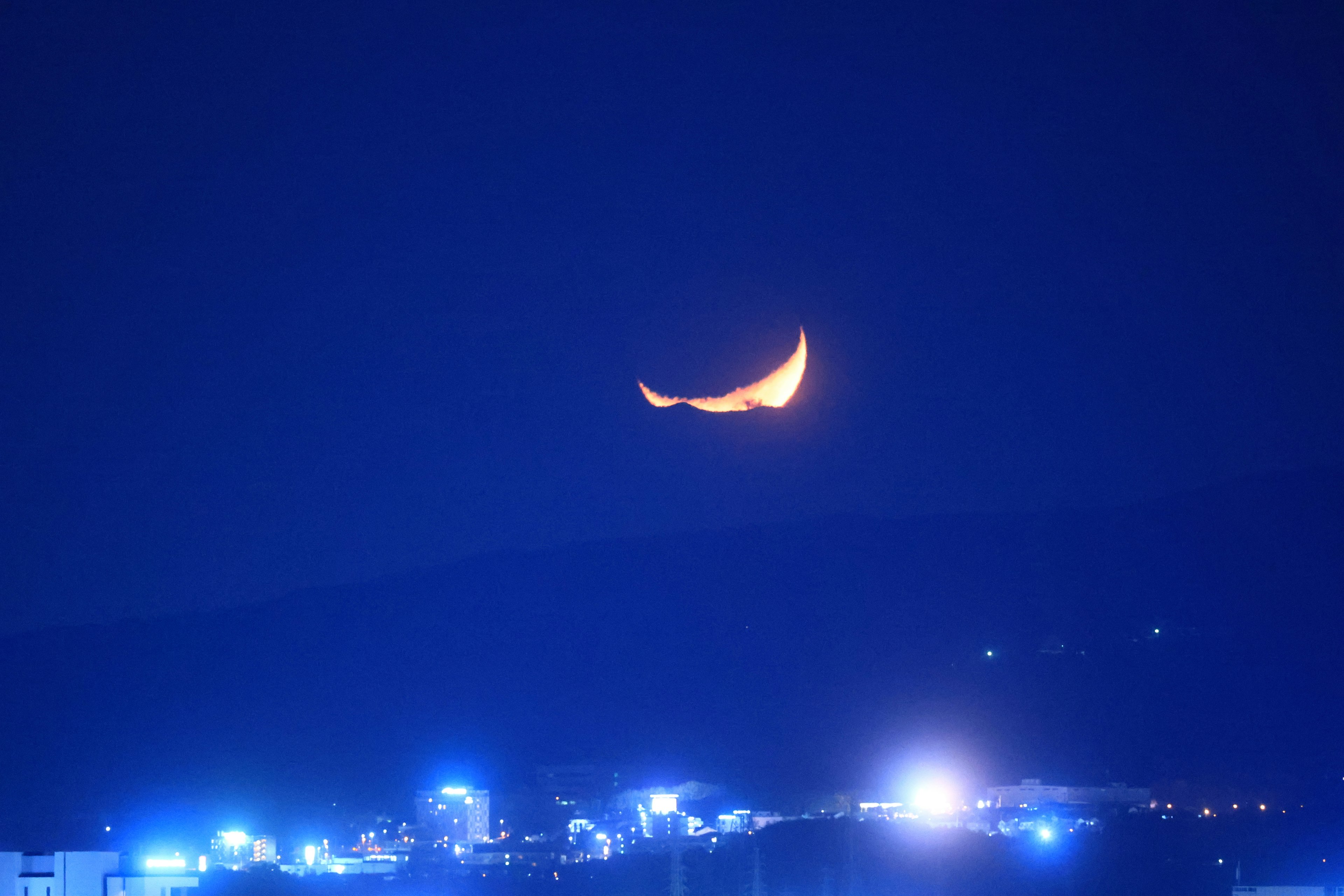 Luna crescente che brilla in un cielo scuro sopra una città con luci blu