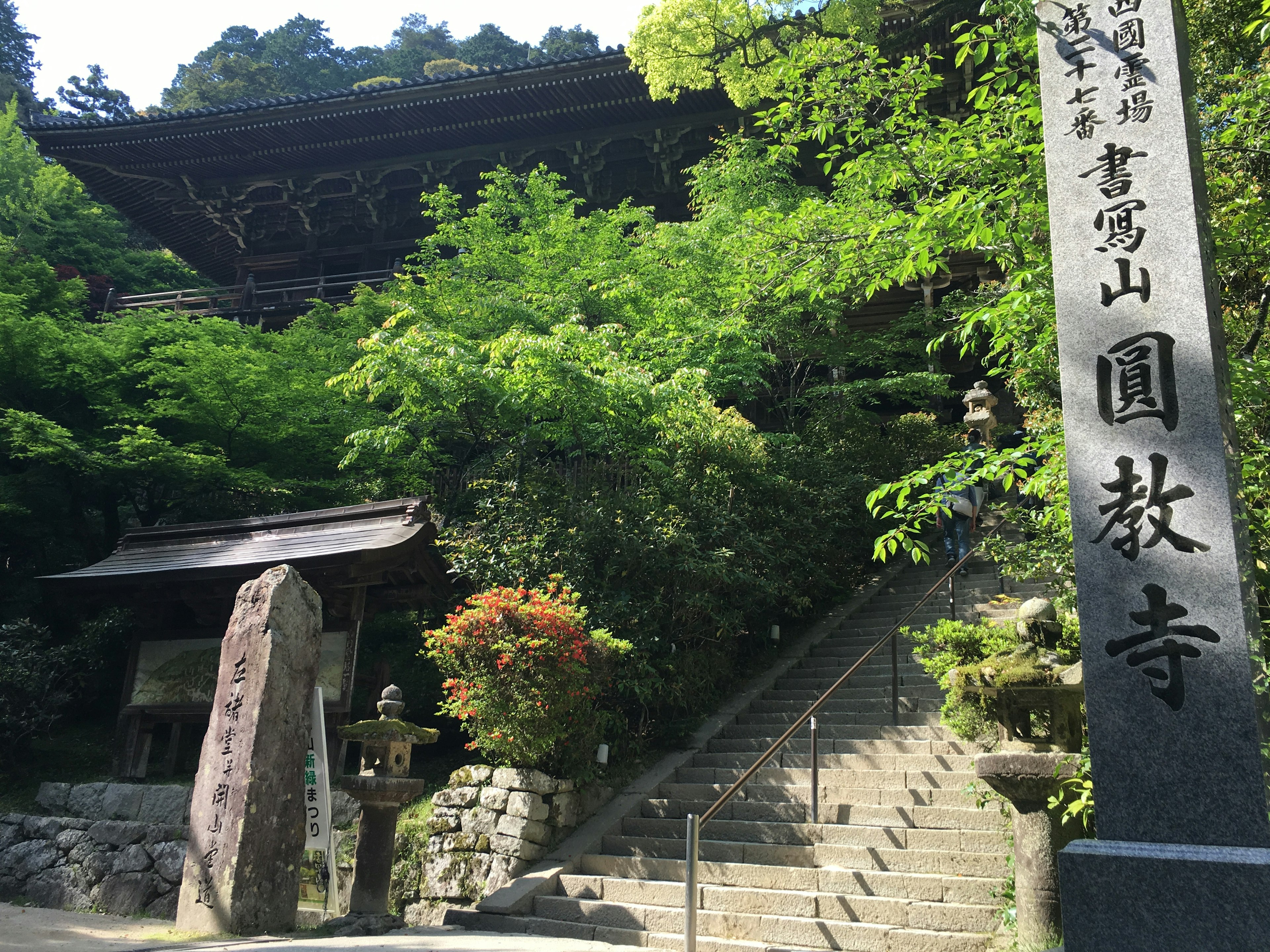 緑に囲まれた寺院の階段と石の標識が特徴的な風景