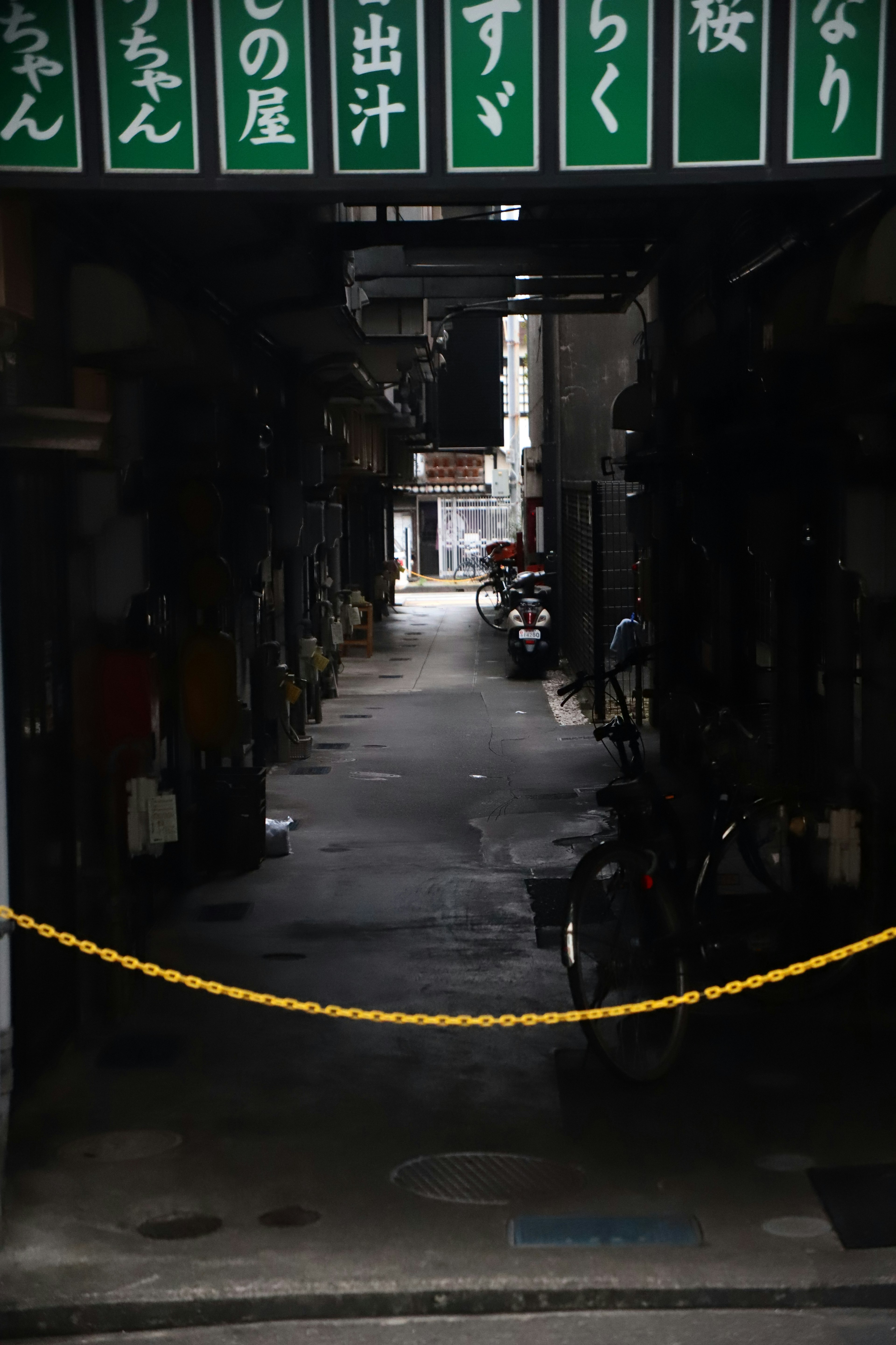 Narrow alley entrance with yellow rope and hanging signs