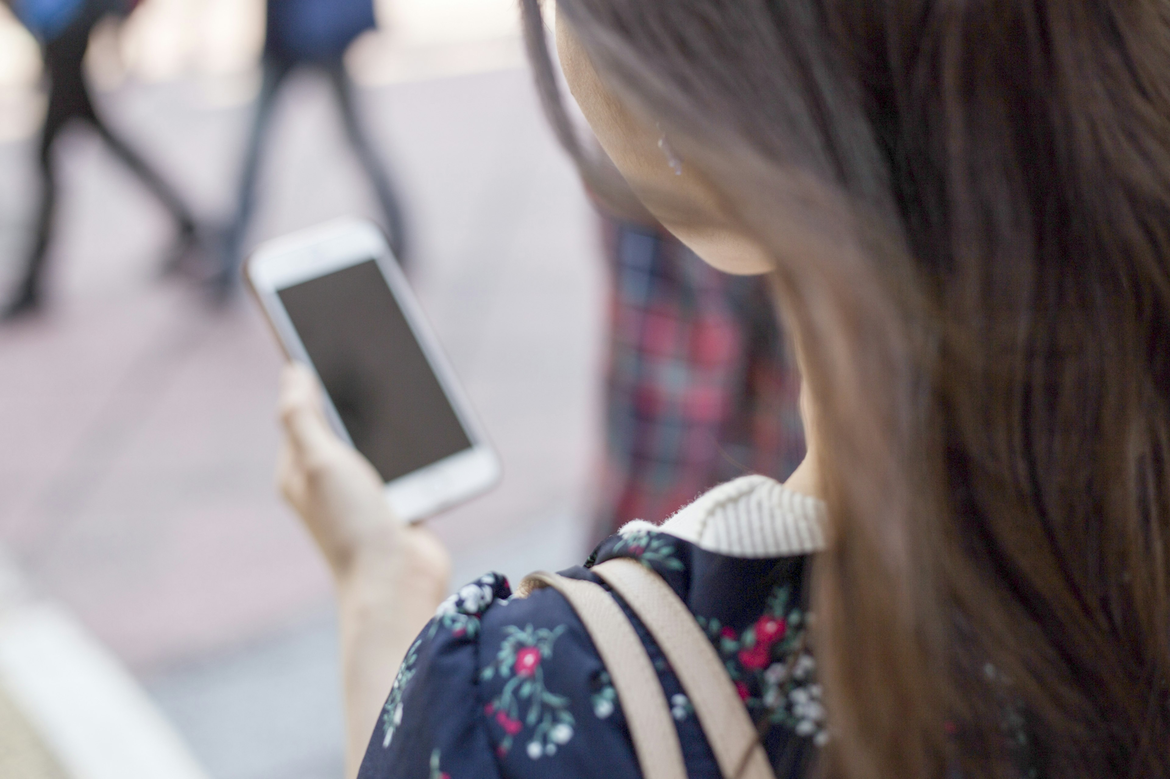 Mujer mirando un smartphone desde atrás rodeada de peatones