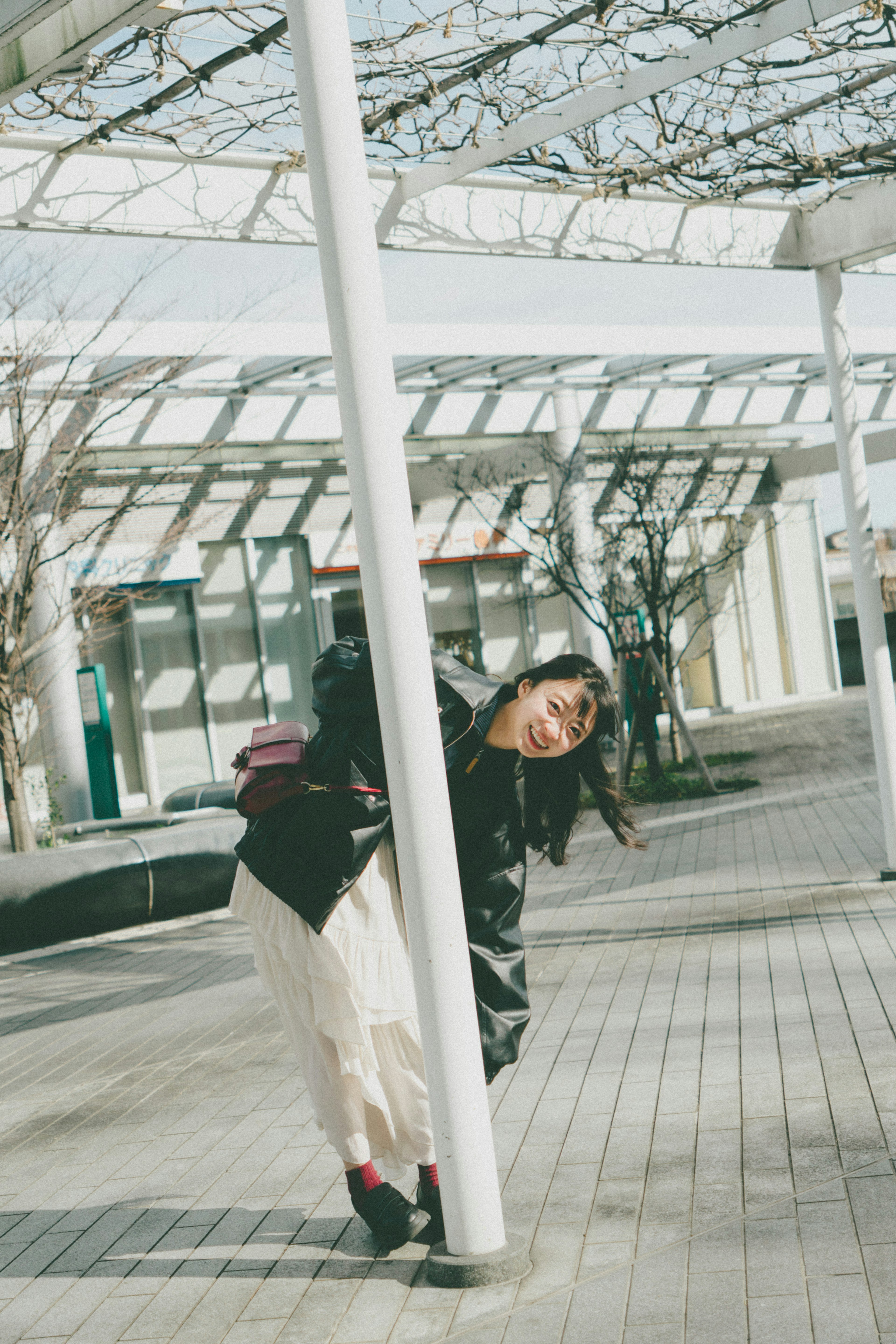 Portrait of a woman peeking behind a pole playful pose in a bright outdoor setting