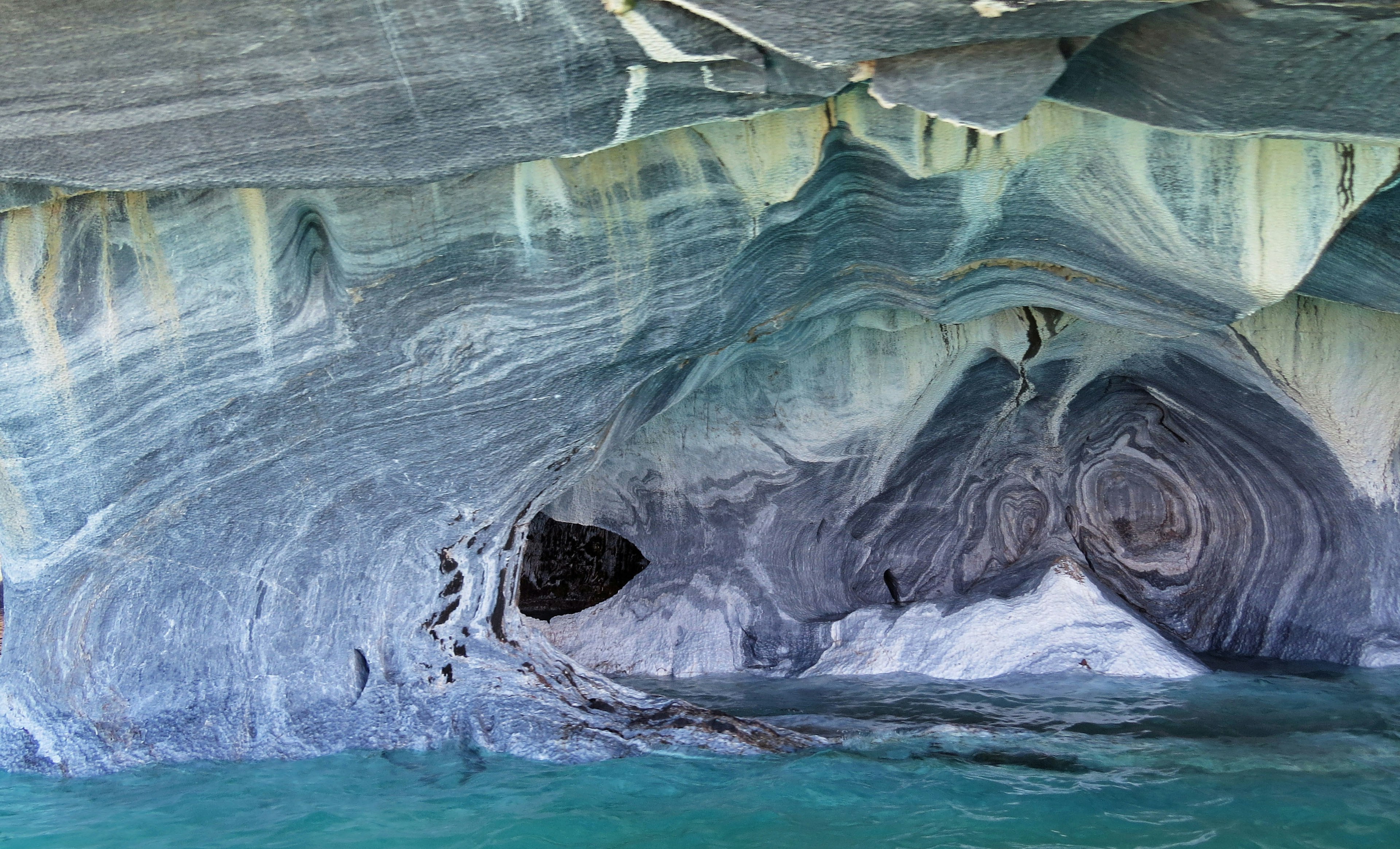 Innenansicht einer Höhle mit blauem Wasser und gestreiften Felsformationen