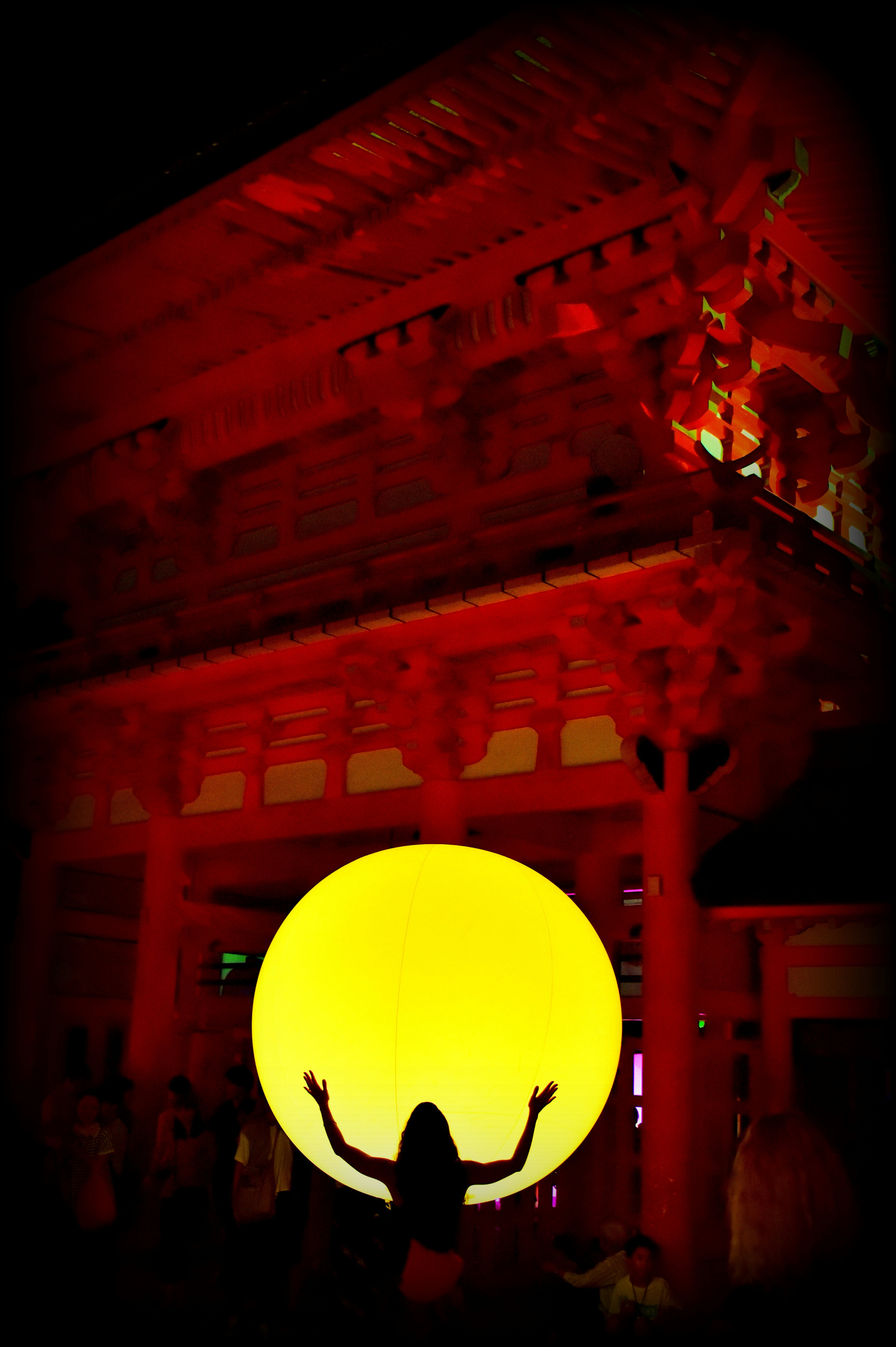 Silhouette of a woman holding a large yellow sphere in front of a red building