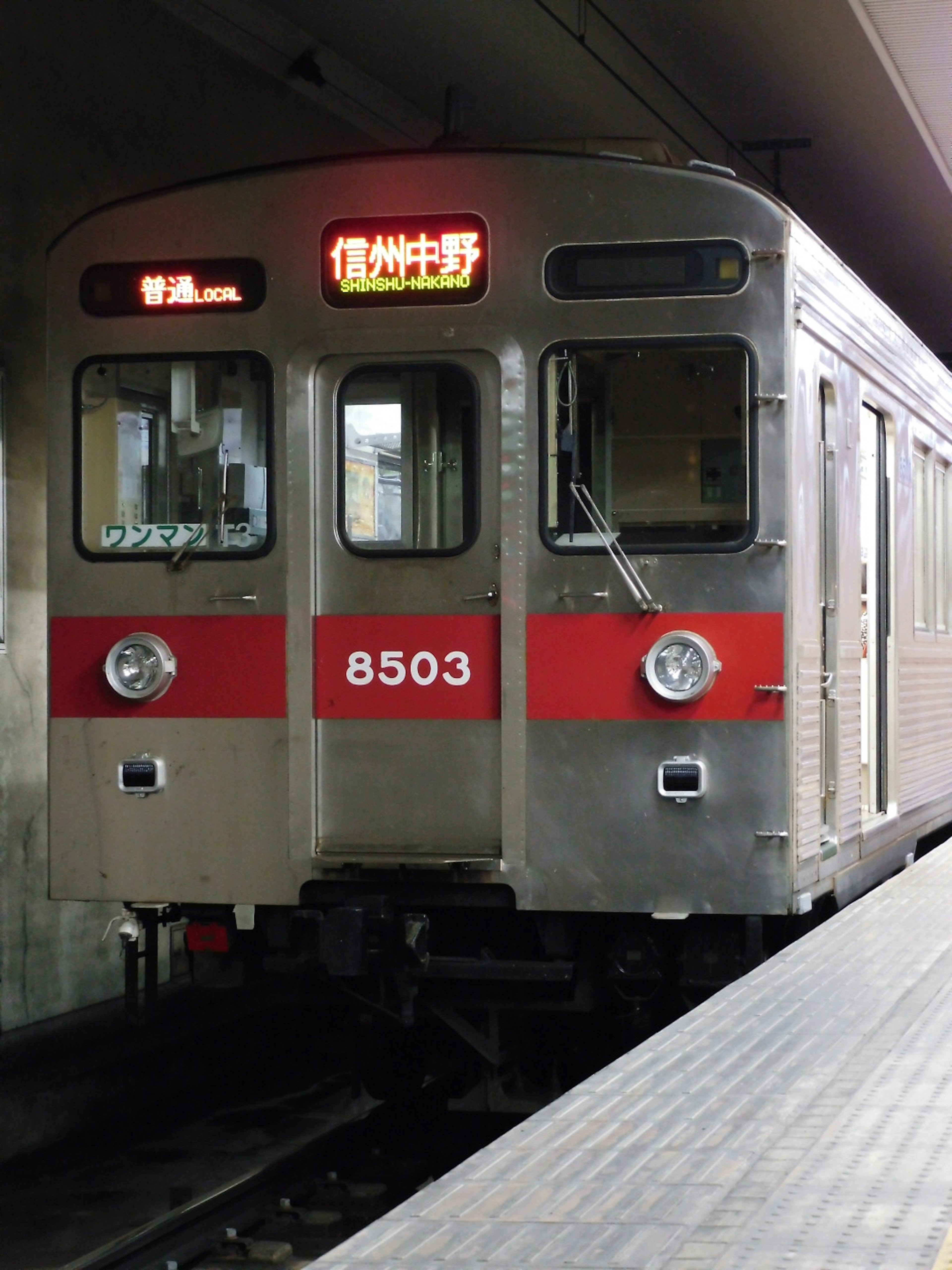 Silver train with red stripes stopped at a station