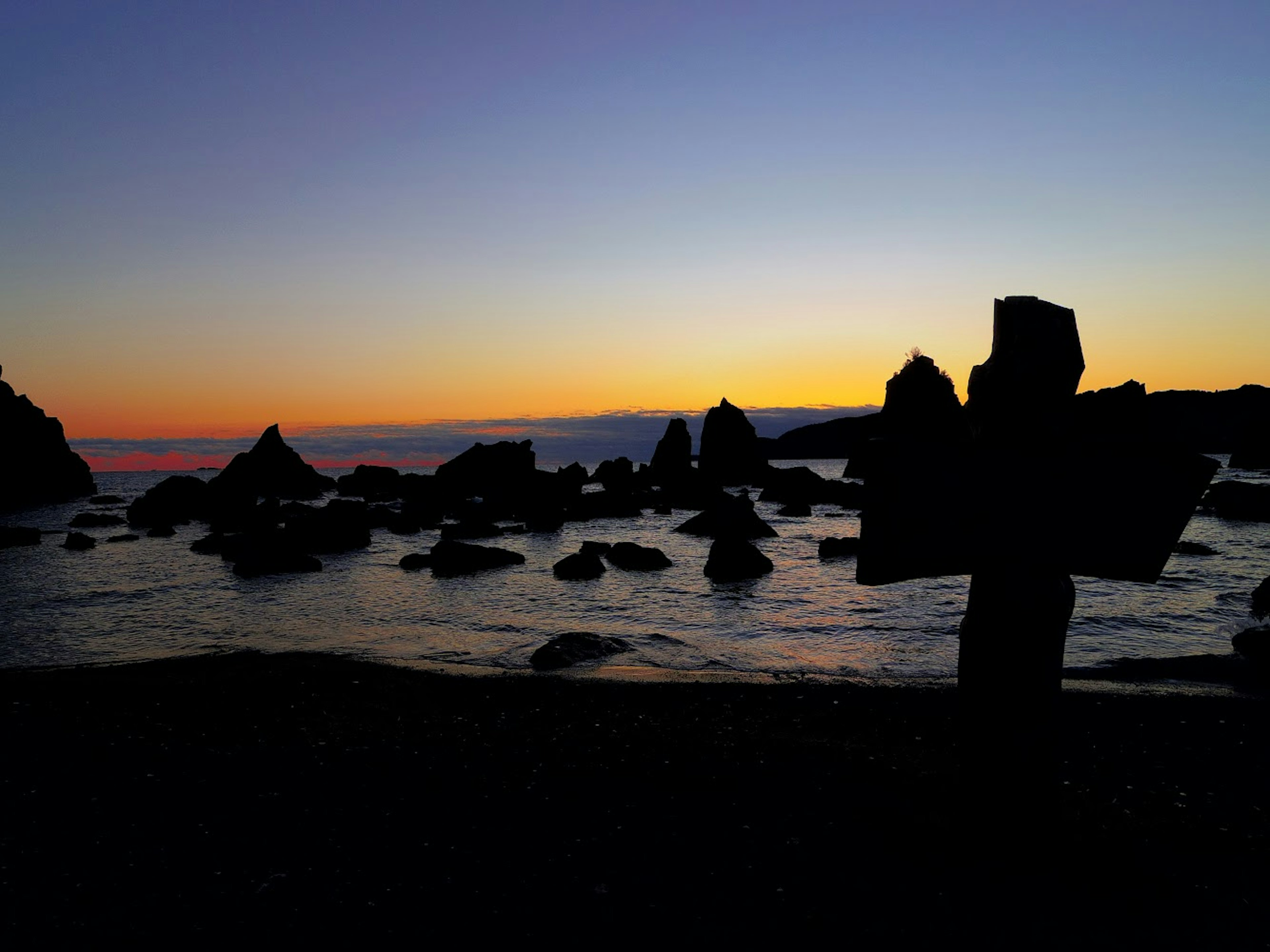 夕焼けの海岸線とシルエットの岩