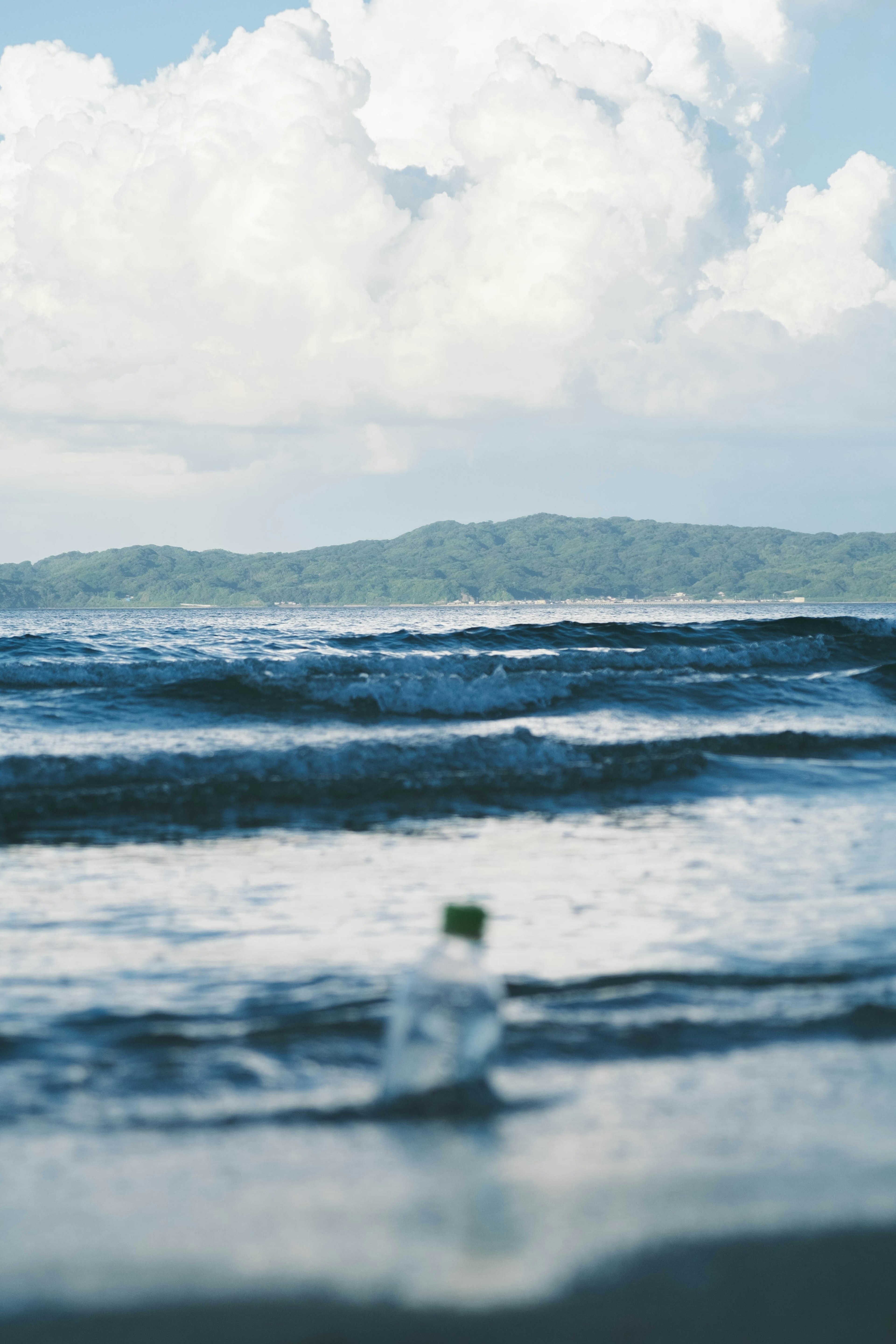 Botella de plástico en la playa con olas y colinas a lo lejos