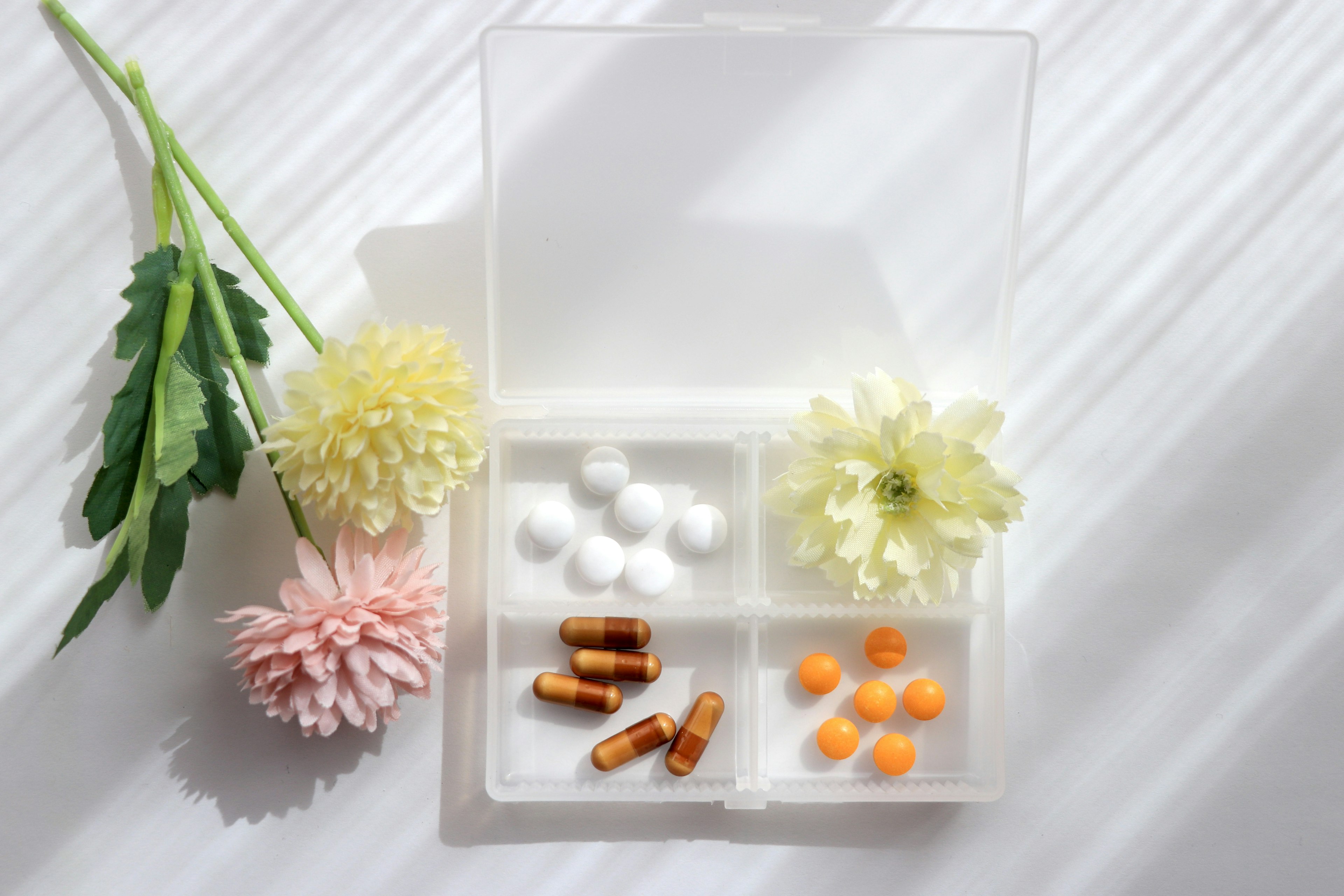 A transparent pill organizer with separated capsules and tablets surrounded by flowers