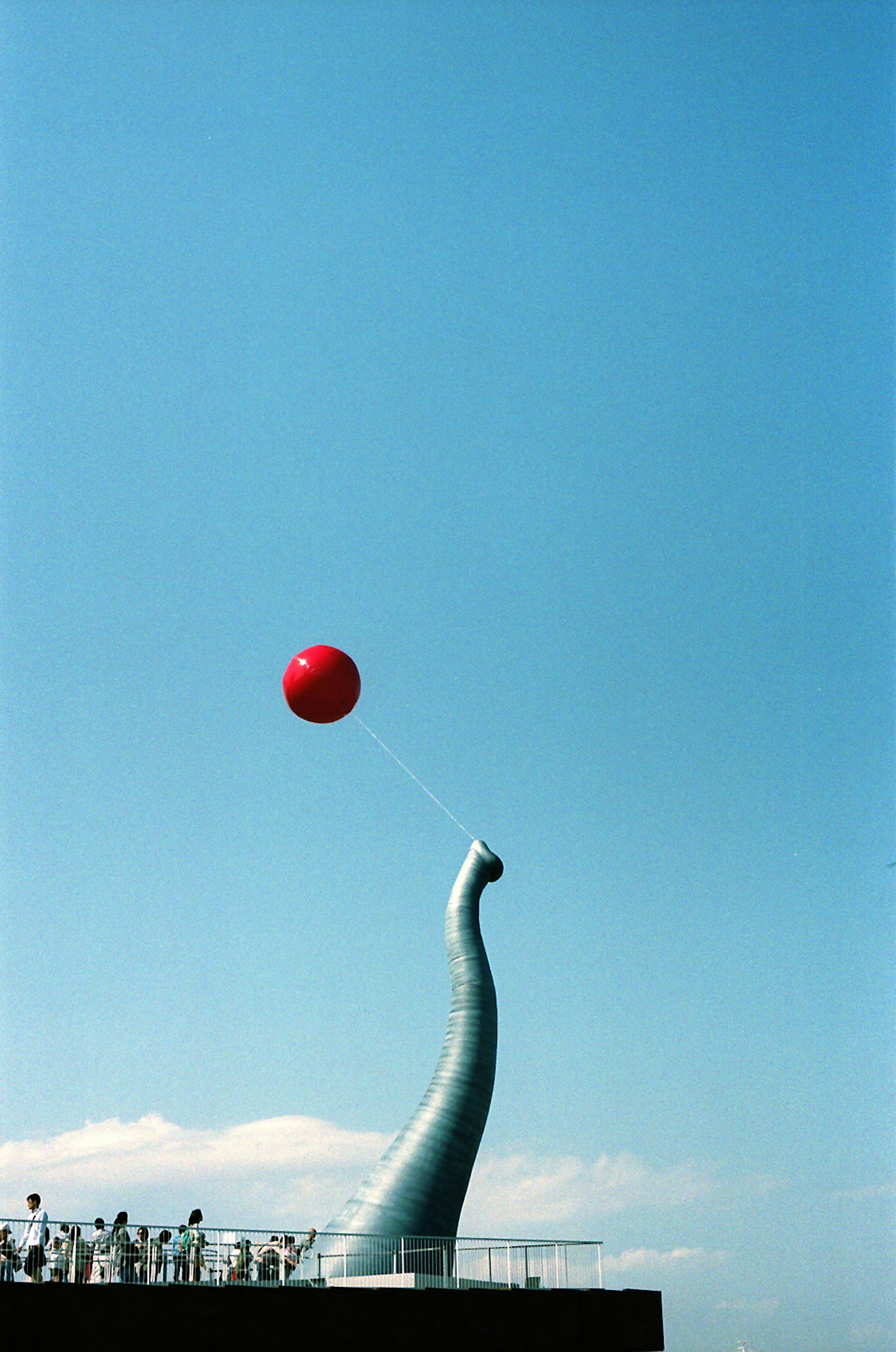 Sculpture with a red balloon against a clear blue sky