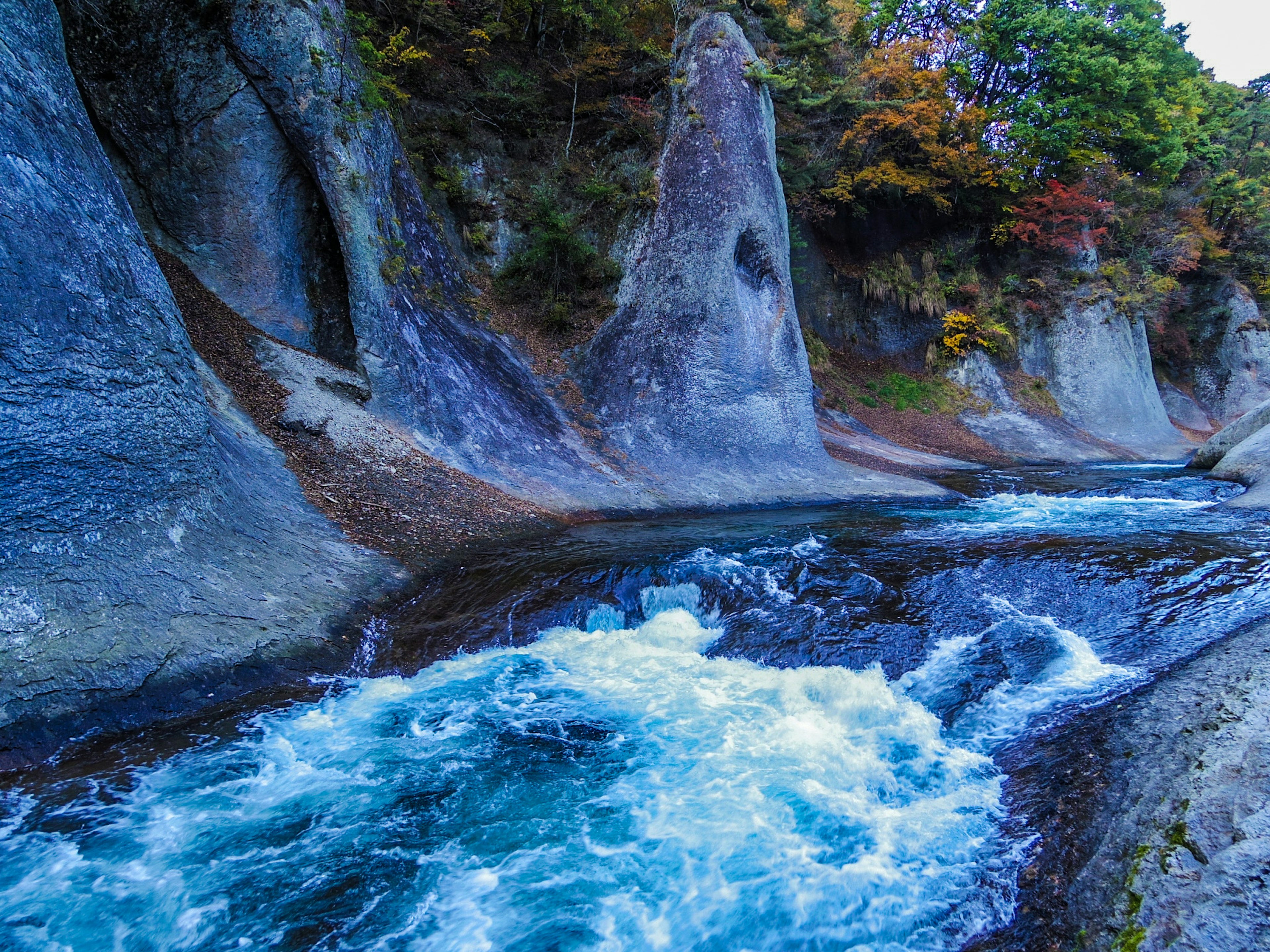 Río azul fluyendo a través de un paisaje rocoso con follaje otoñal