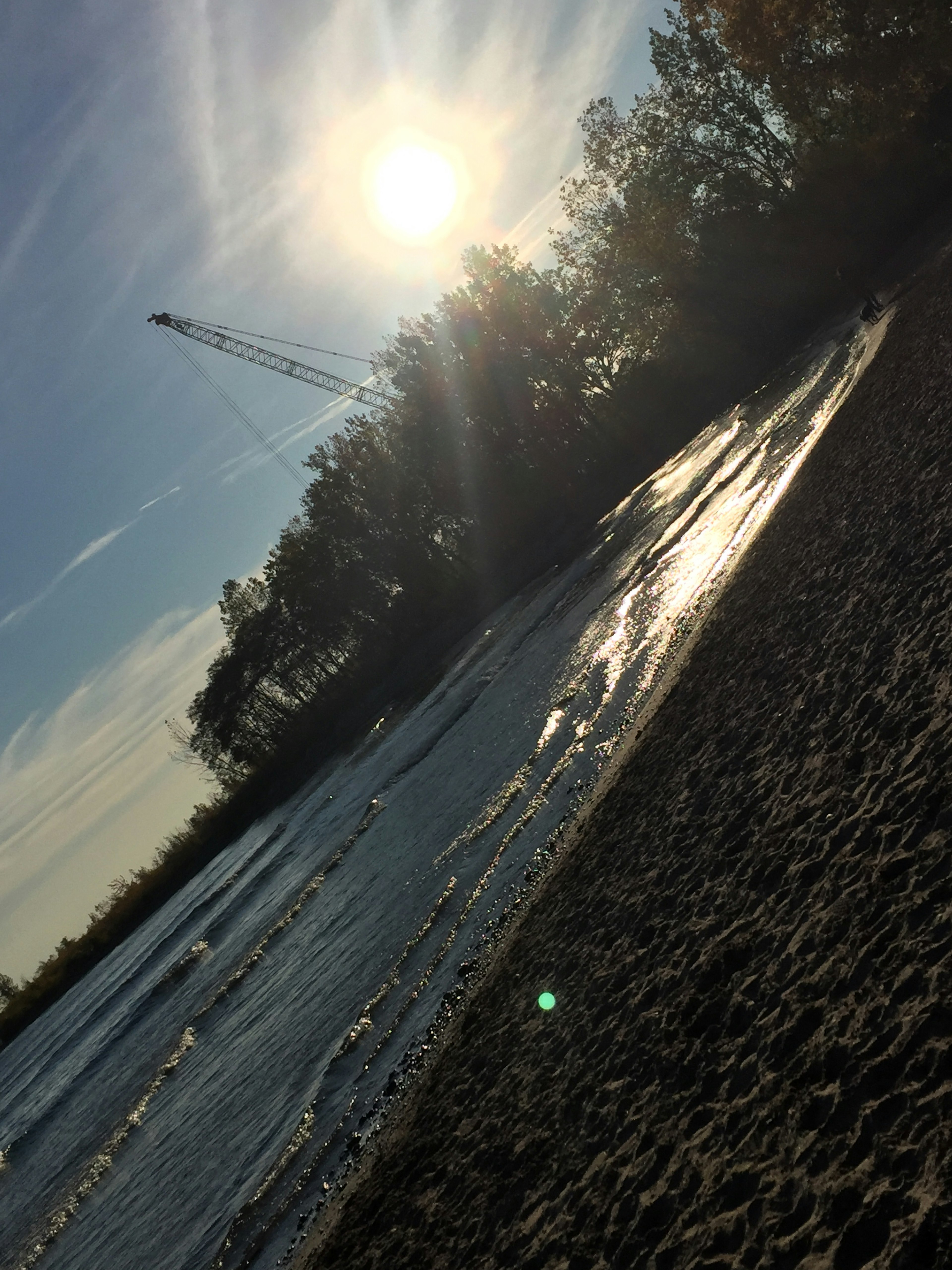 Pantai berpasir di tepi sungai dengan air mengalir di bawah sinar matahari yang cerah dan langit biru