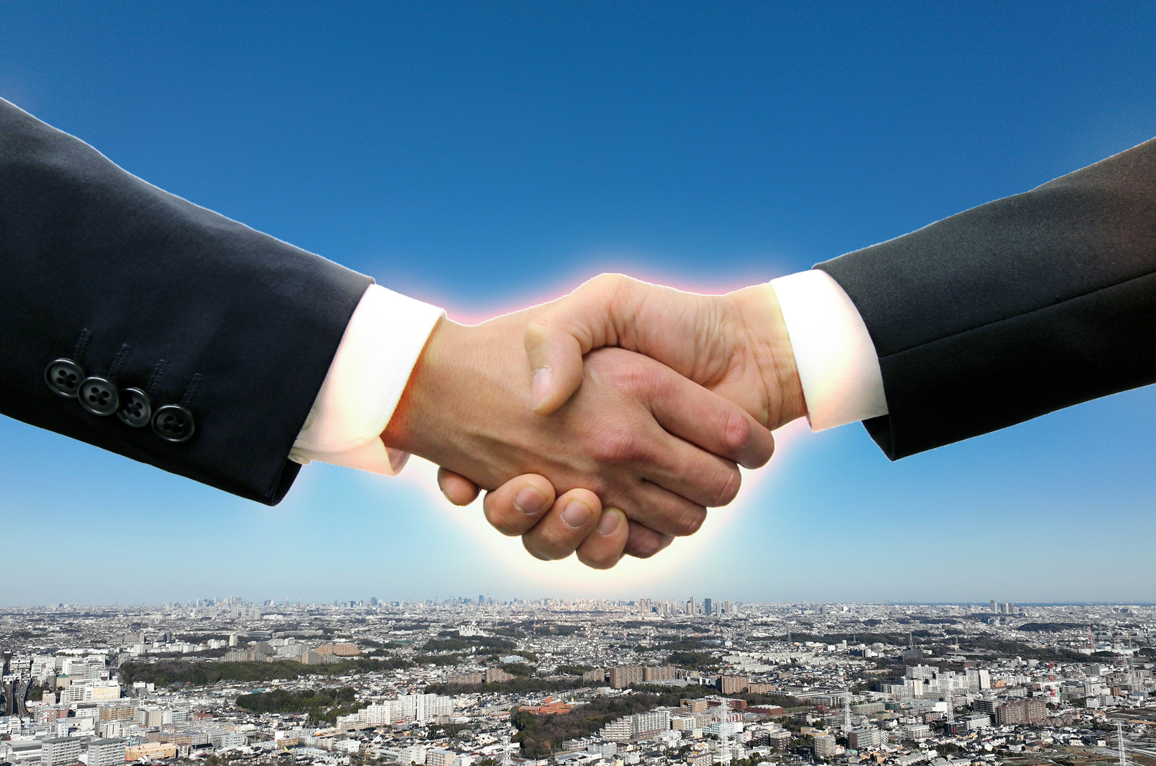 Image of two hands shaking in business suits against a blue sky