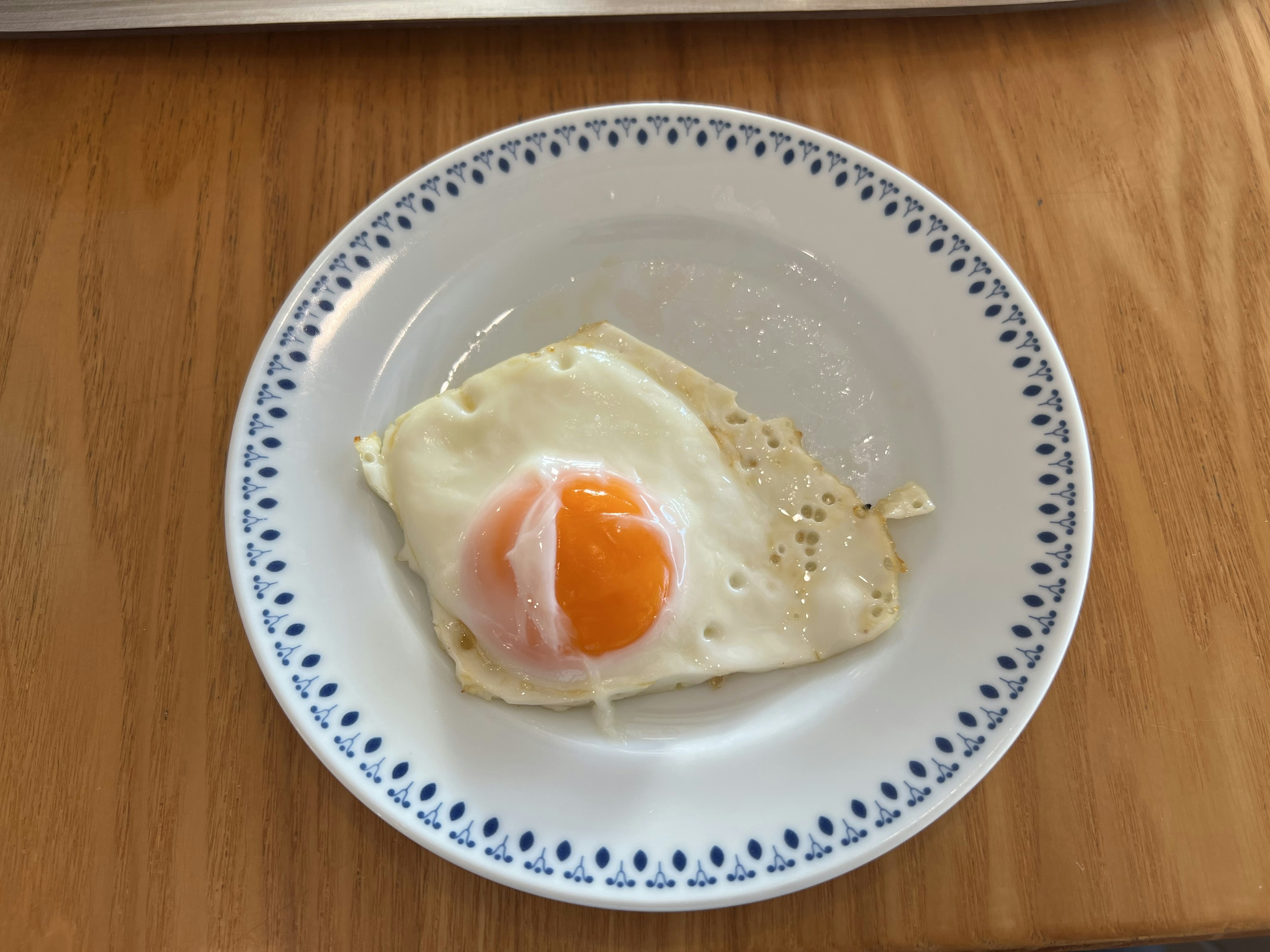 Un huevo frito en un plato blanco con borde decorativo