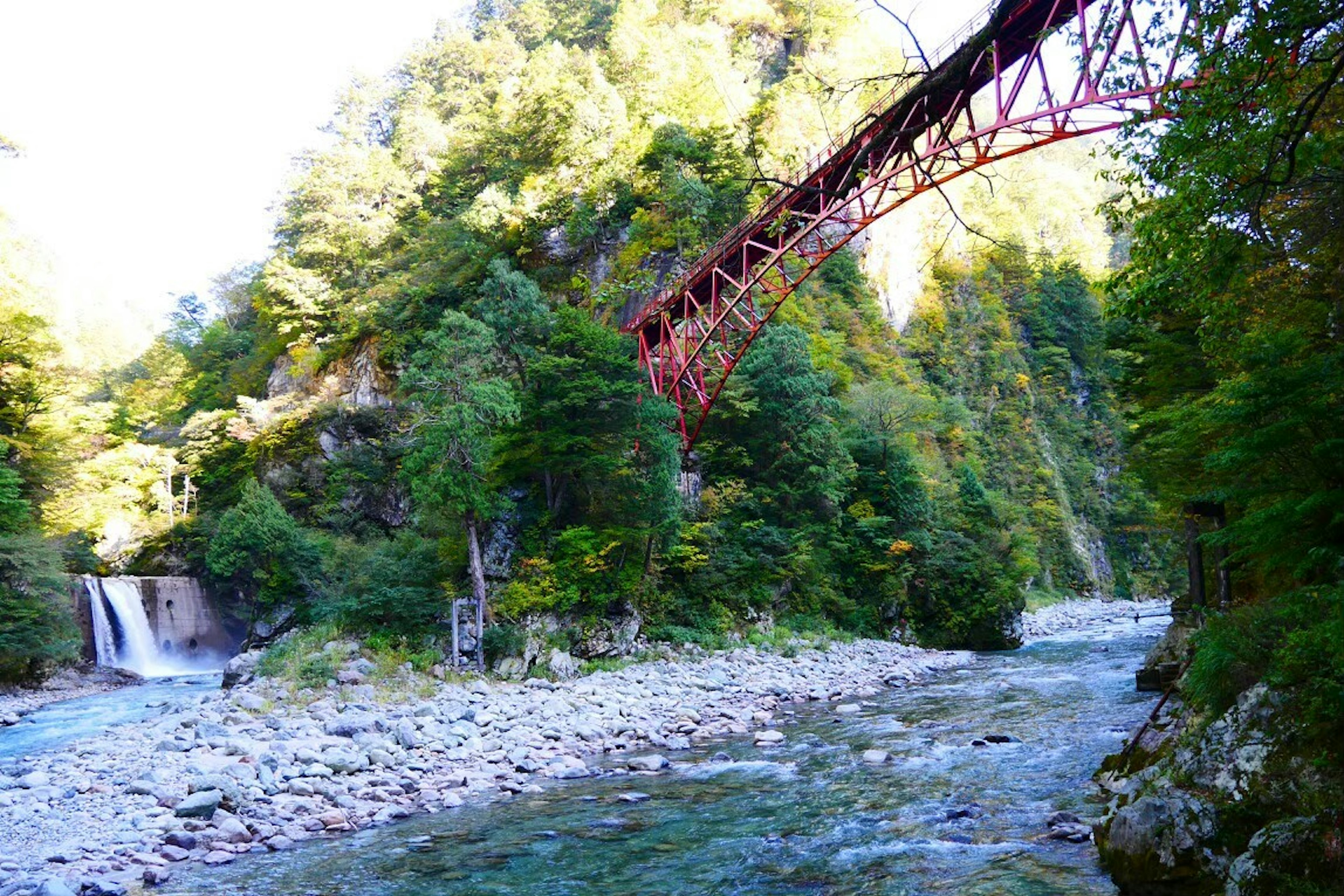 Scenic view of a red iron bridge over a clear blue river in a lush green valley