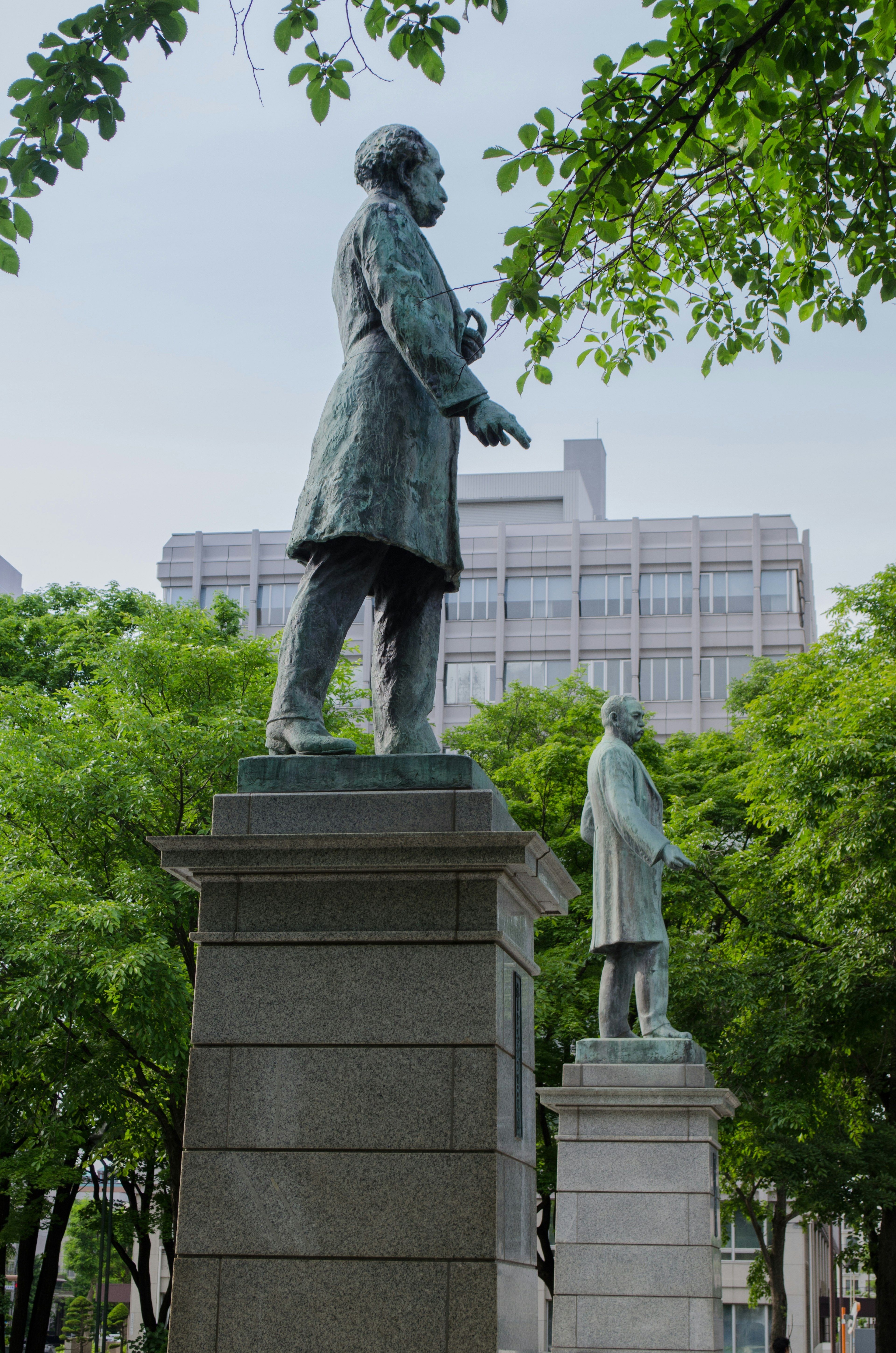 Two bronze statues standing in a park surrounded by green trees