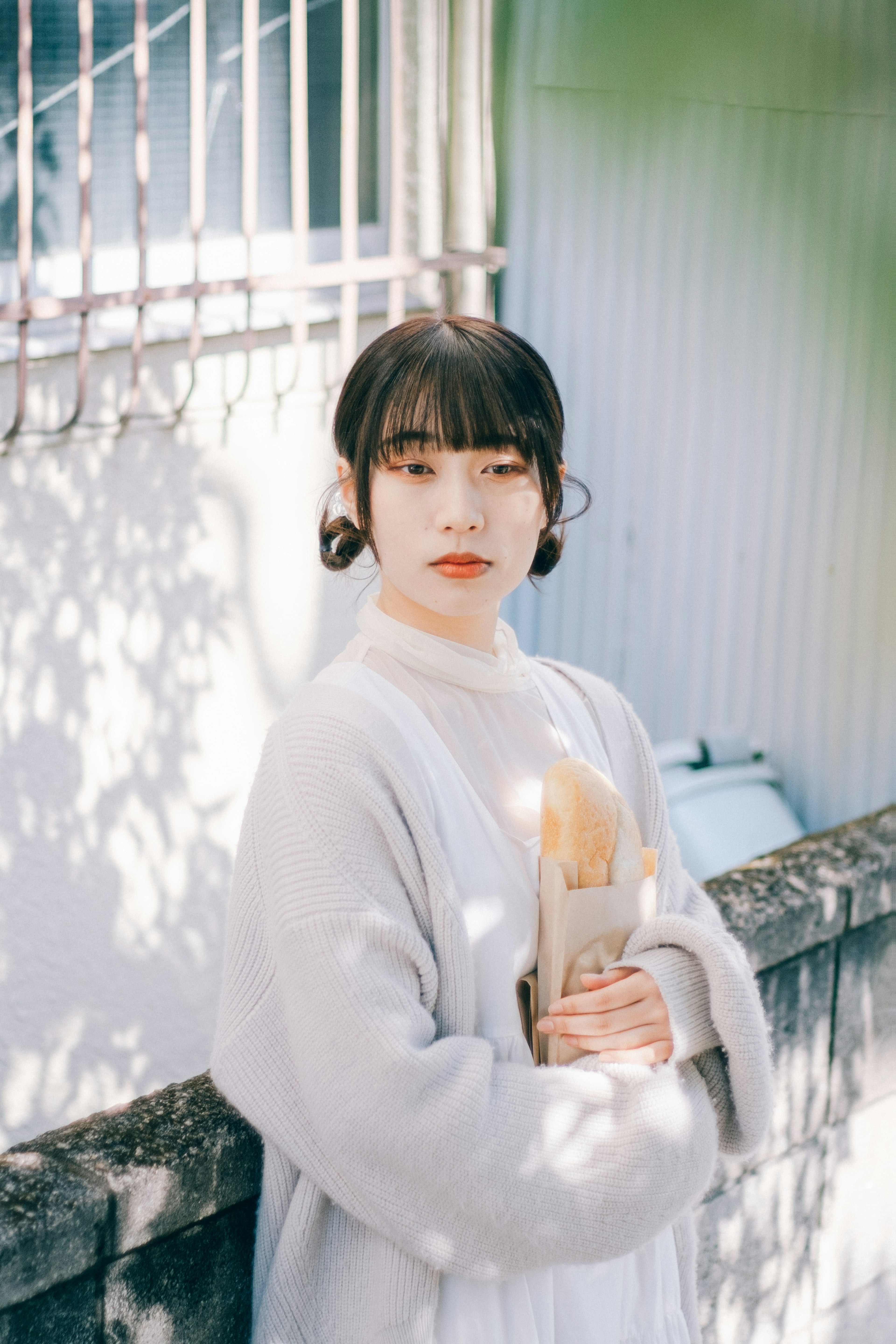 A woman in a gray sweater is posing with a gentle expression while holding a bouquet with dappled sunlight creating shadows in the background