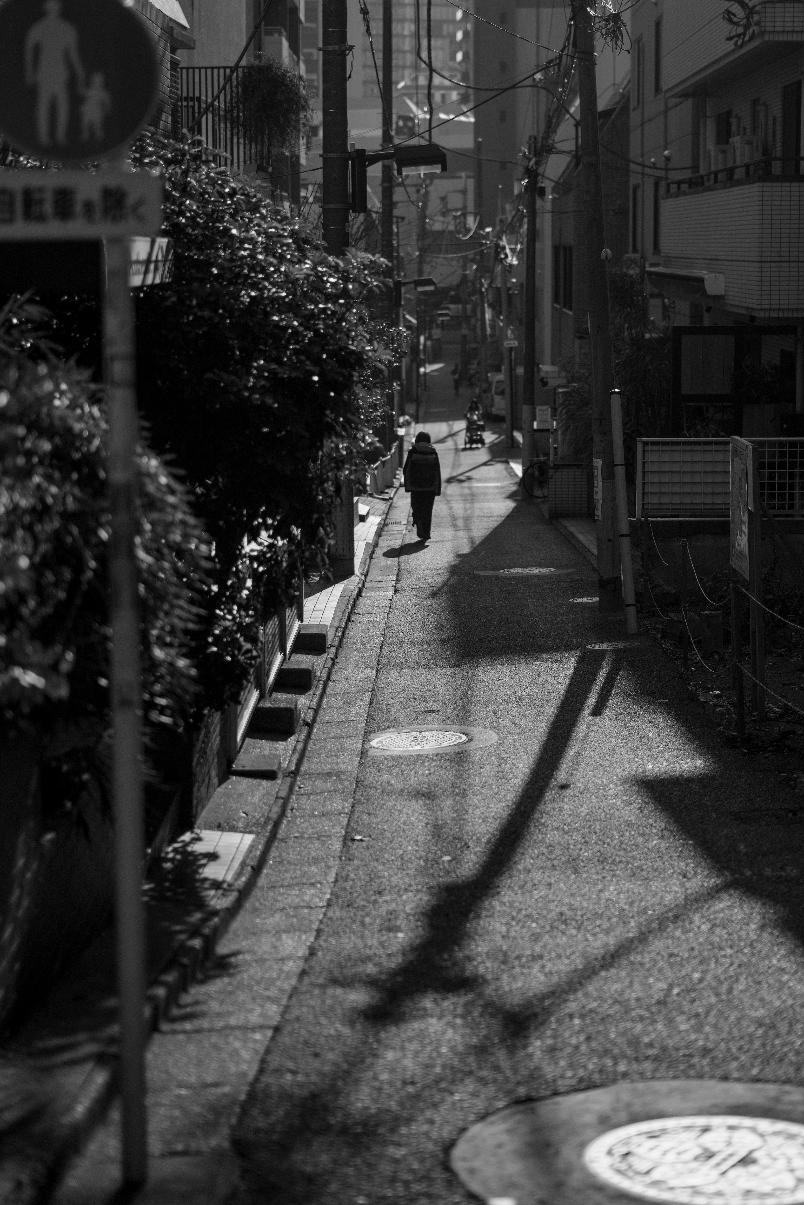 Black and white photo of a person walking down a quiet alley