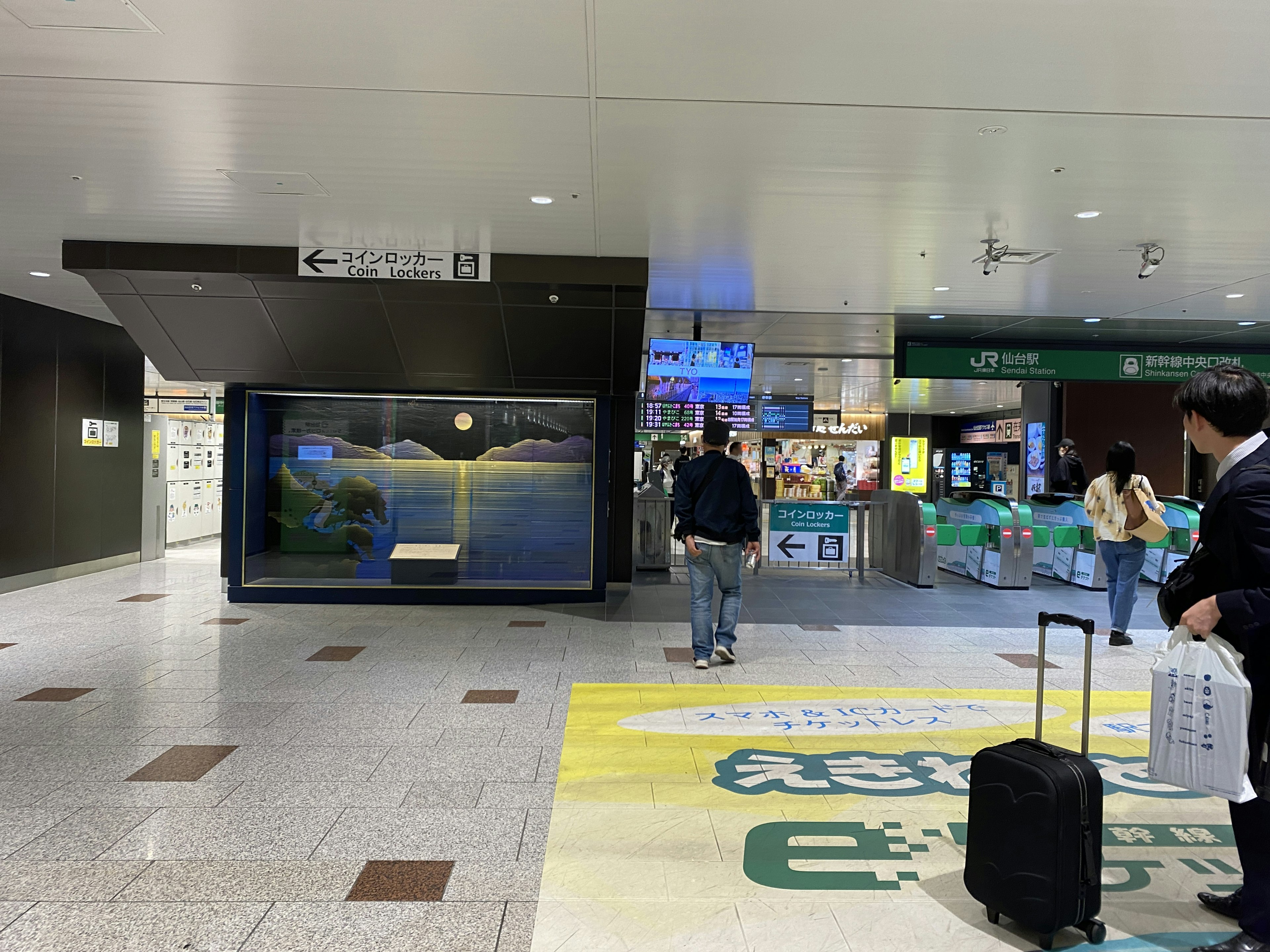 Interior view of a train station with people walking and digital signage visible