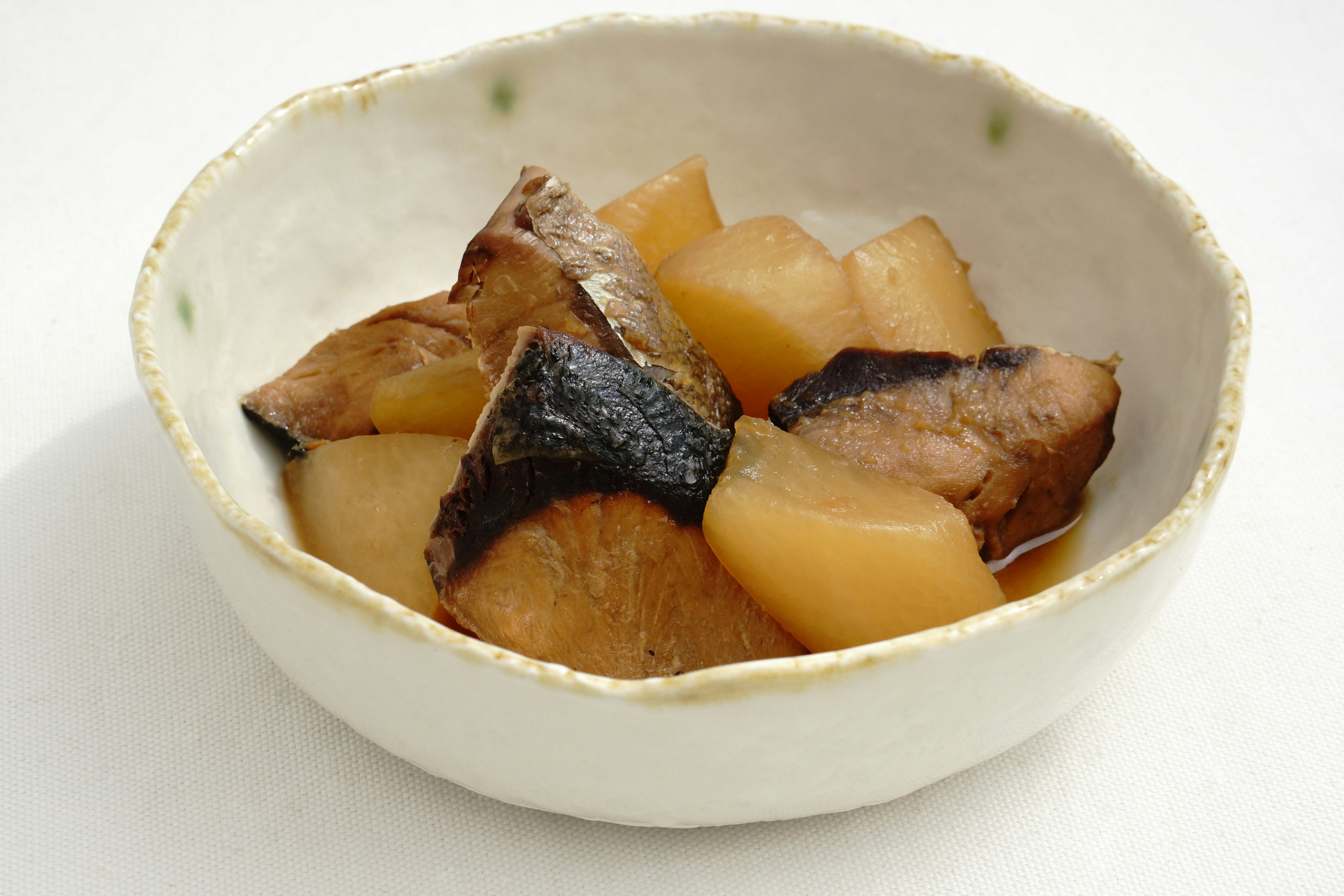 Un plato de caballa y rábano daikon cocidos servido en un bol blanco