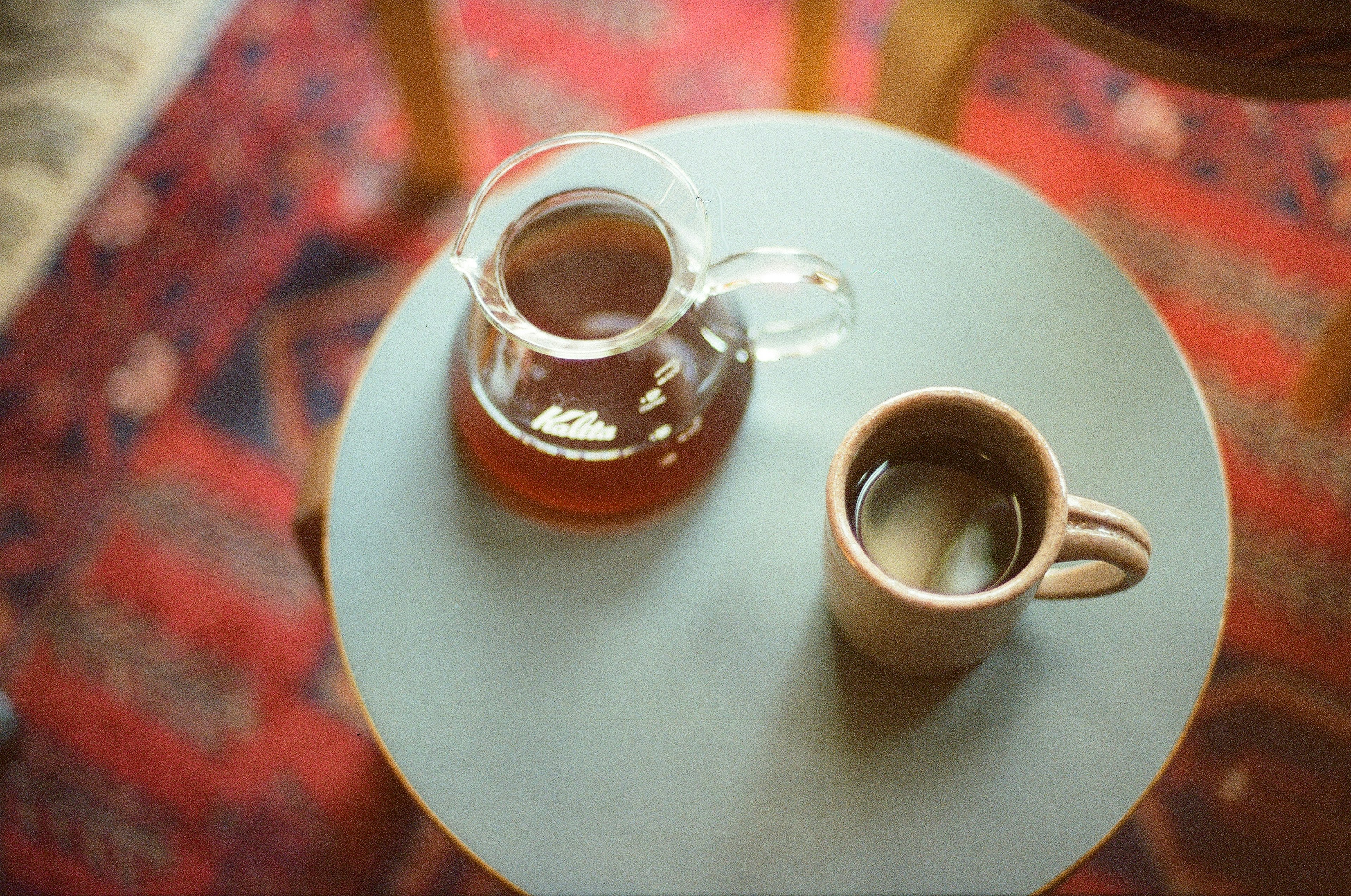 Cafetera transparente y taza de cerámica sobre una mesa