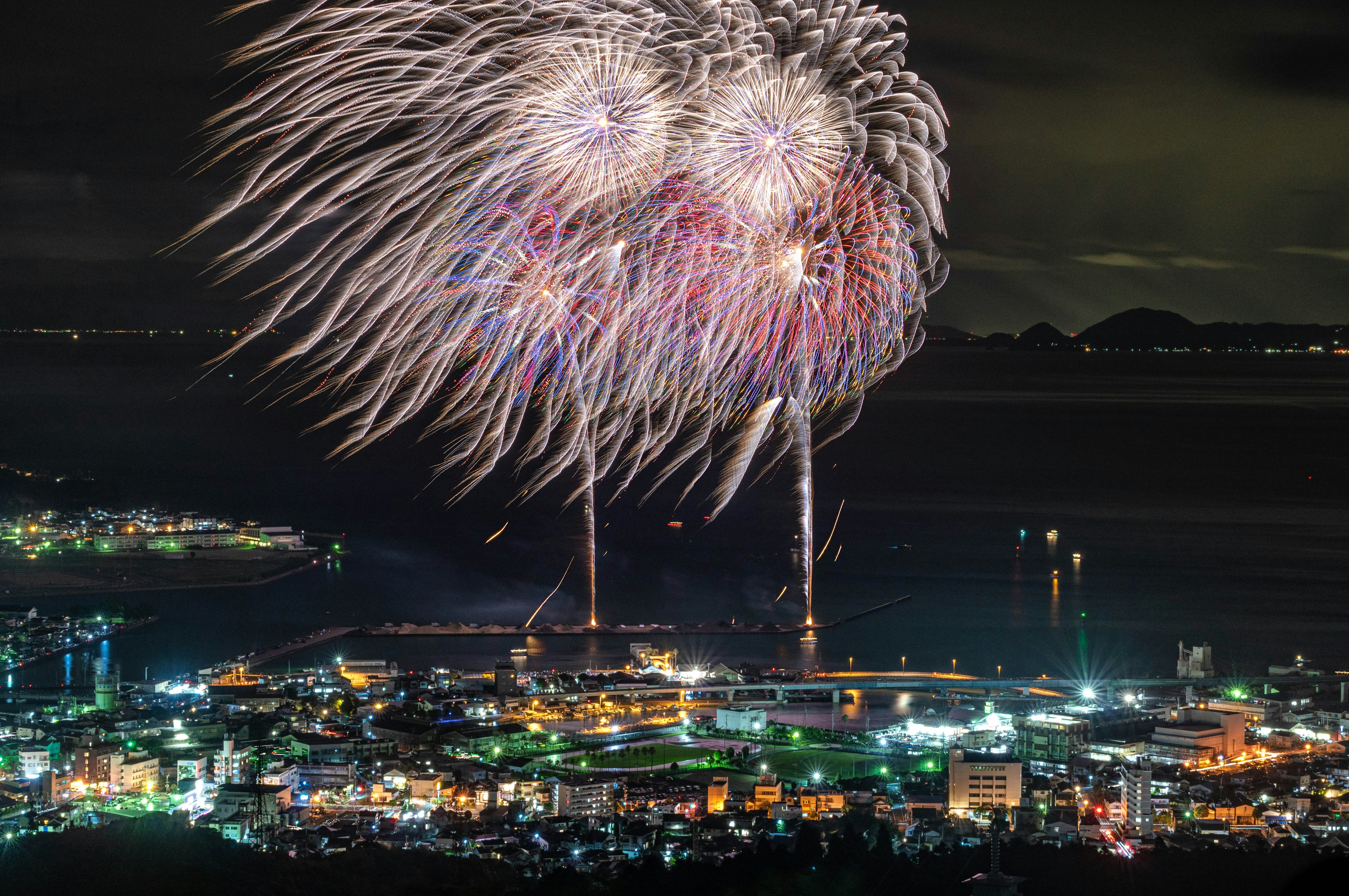 Fuochi d'artificio colorati illuminano il cielo notturno sopra una città costiera