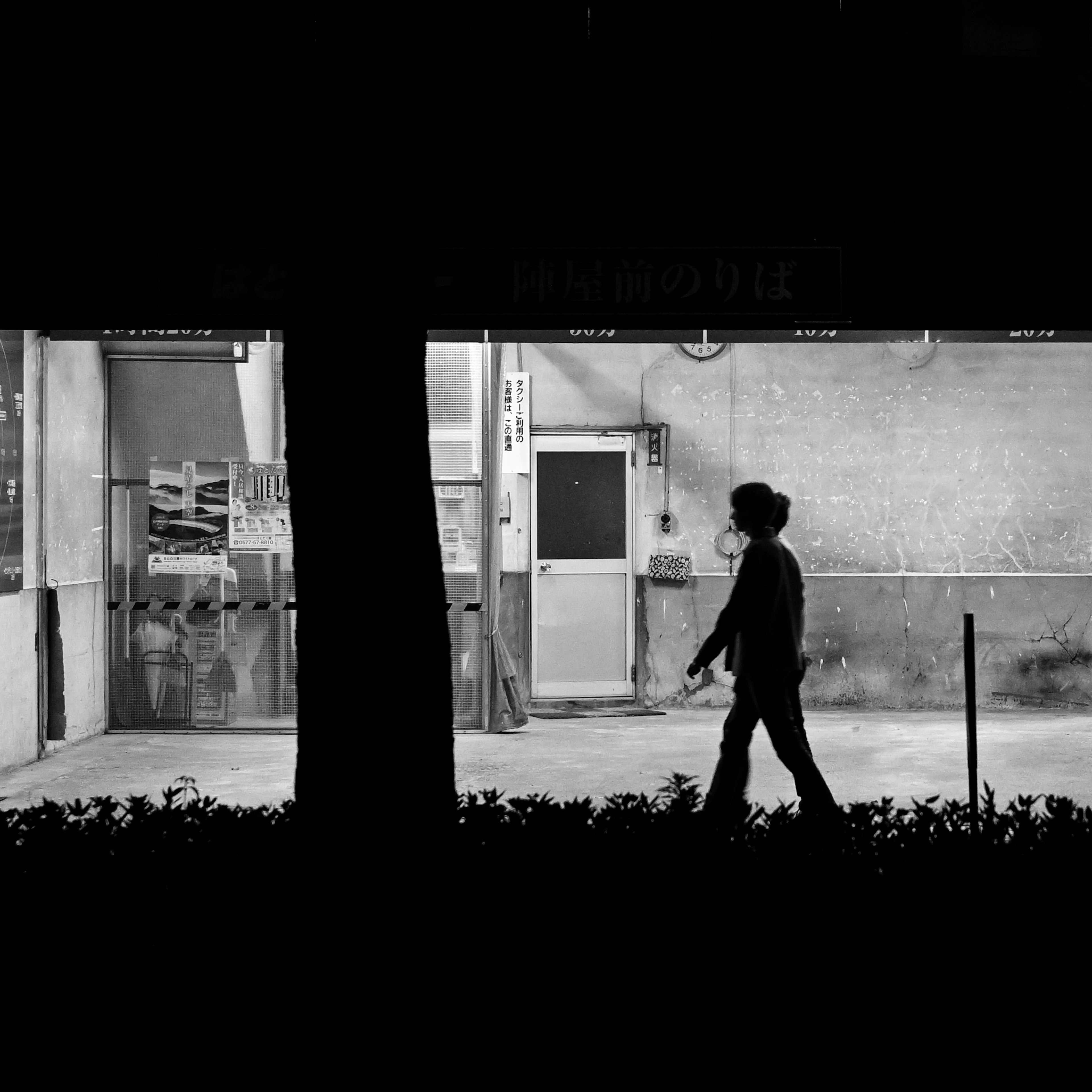 Silhouette of a person walking past a brightly lit store at night