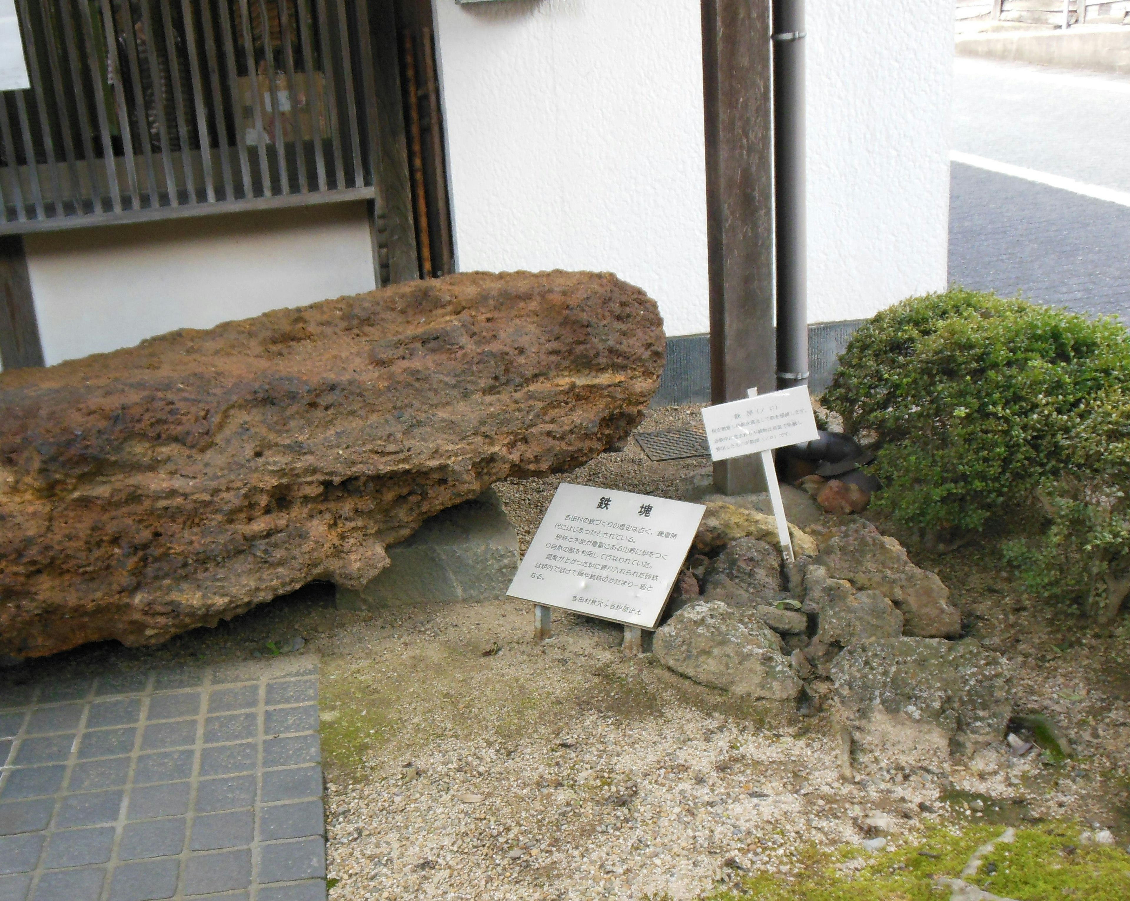 A large rock sculpture with informational plaques in front of a traditional Japanese building